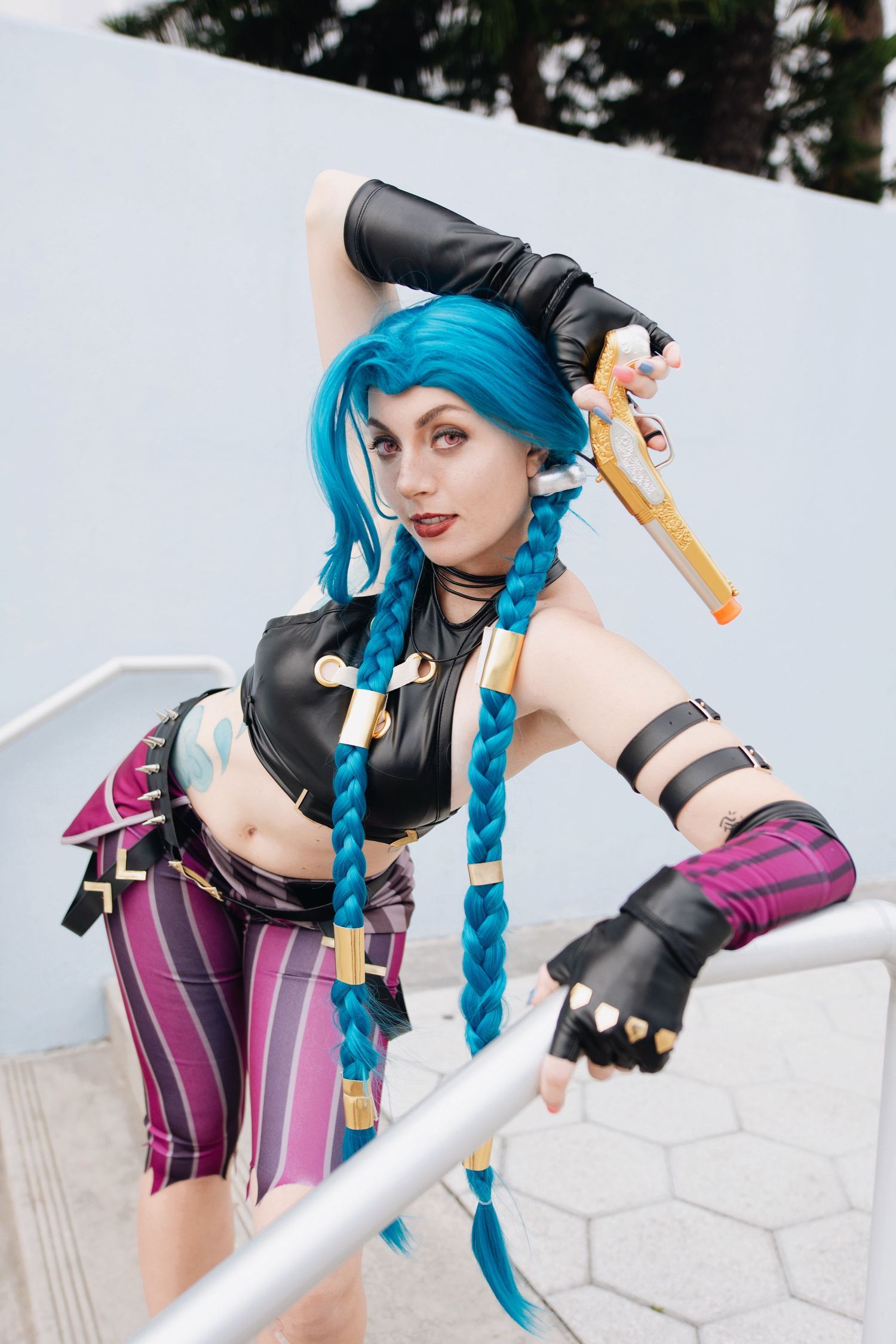 Anime cosplayer with bright blue braids and combat outfit strikes fighting stance.