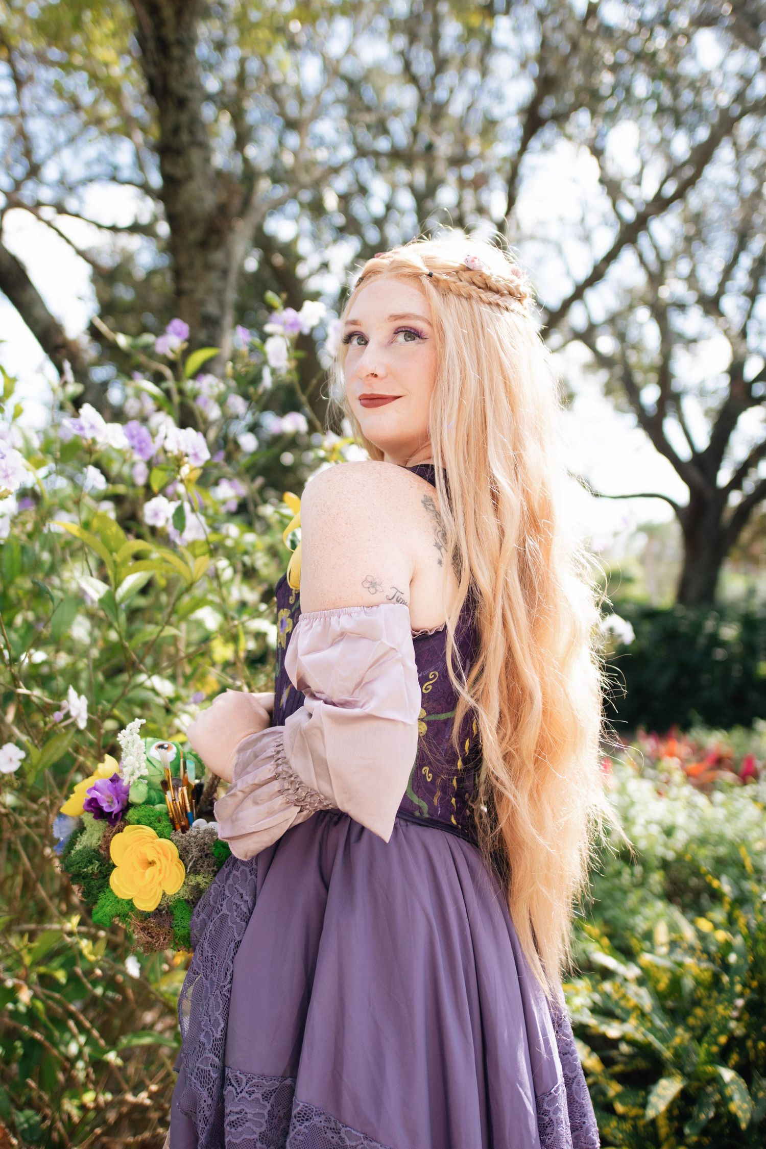 A flowing purple renaissance dress with off-shoulder sleeves photographed in a blooming garden.