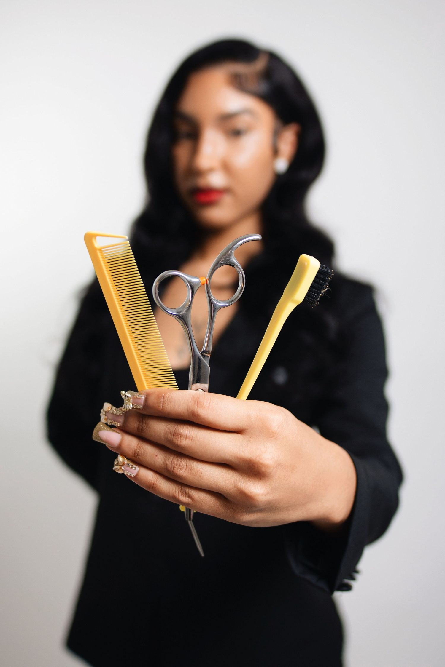 Professional hairstylist holding gold combs and scissors against white background.