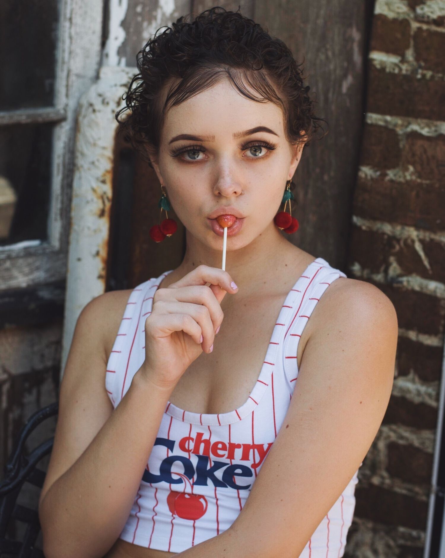 Retro-inspired portrait series with pinstripe tank top and cherry lollipop against brick wall.