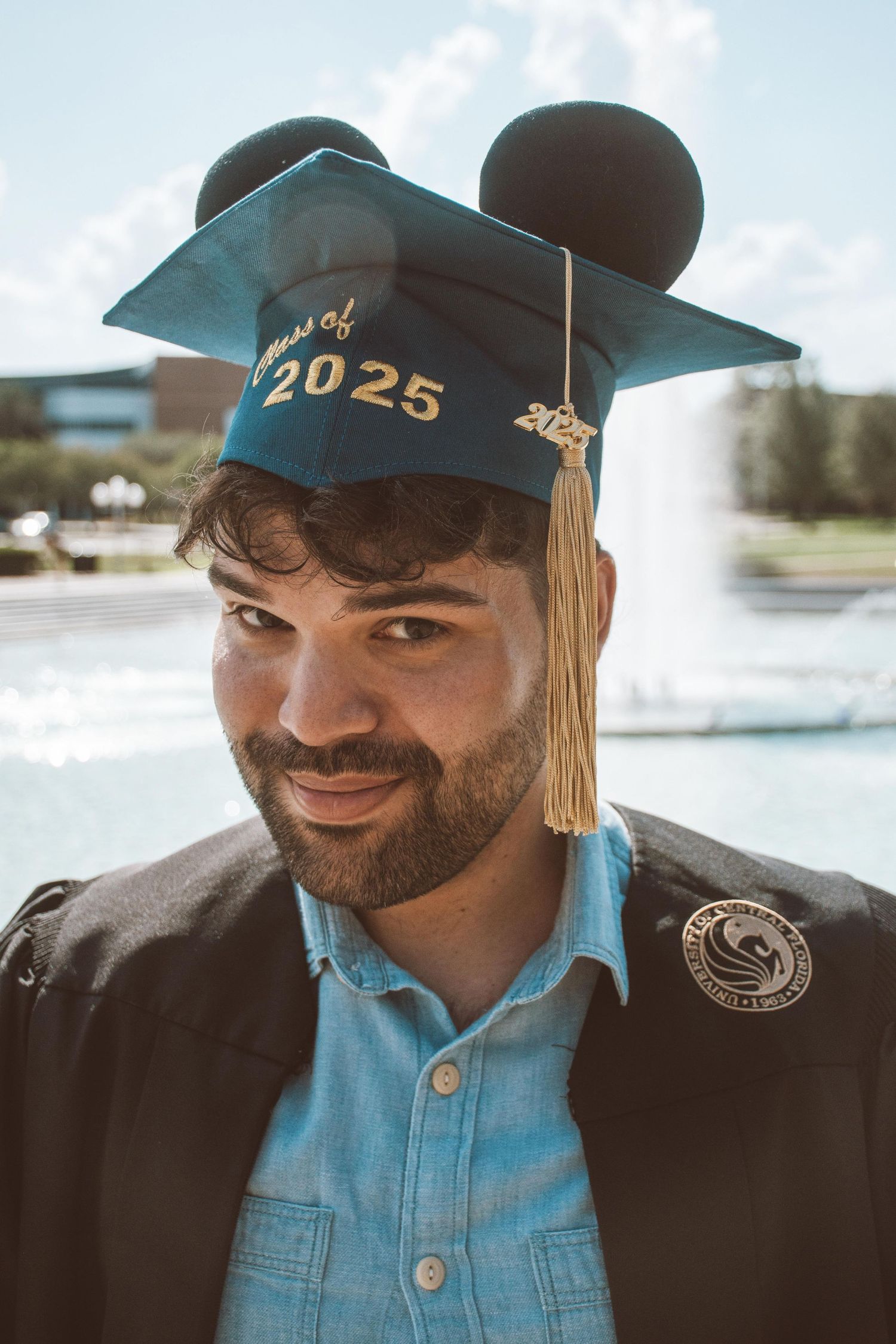 Graduate wearing class of 2025 cap smiles in front of waterfront setting.