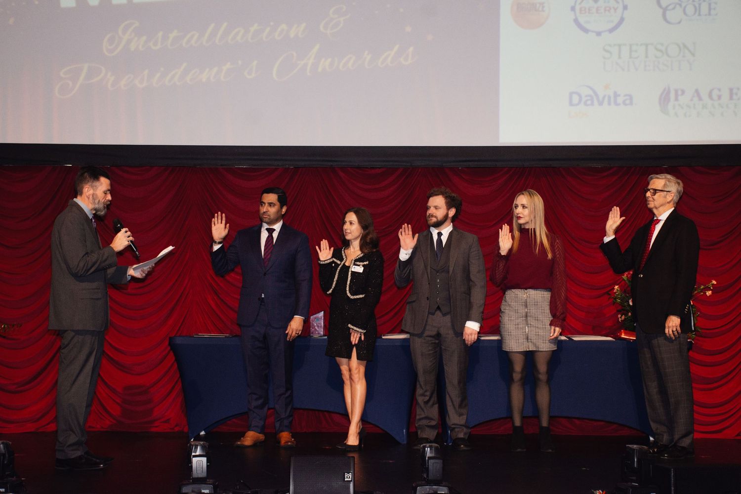 People standing together on a red carpeted stage during what appears to be a formal event or ceremony.