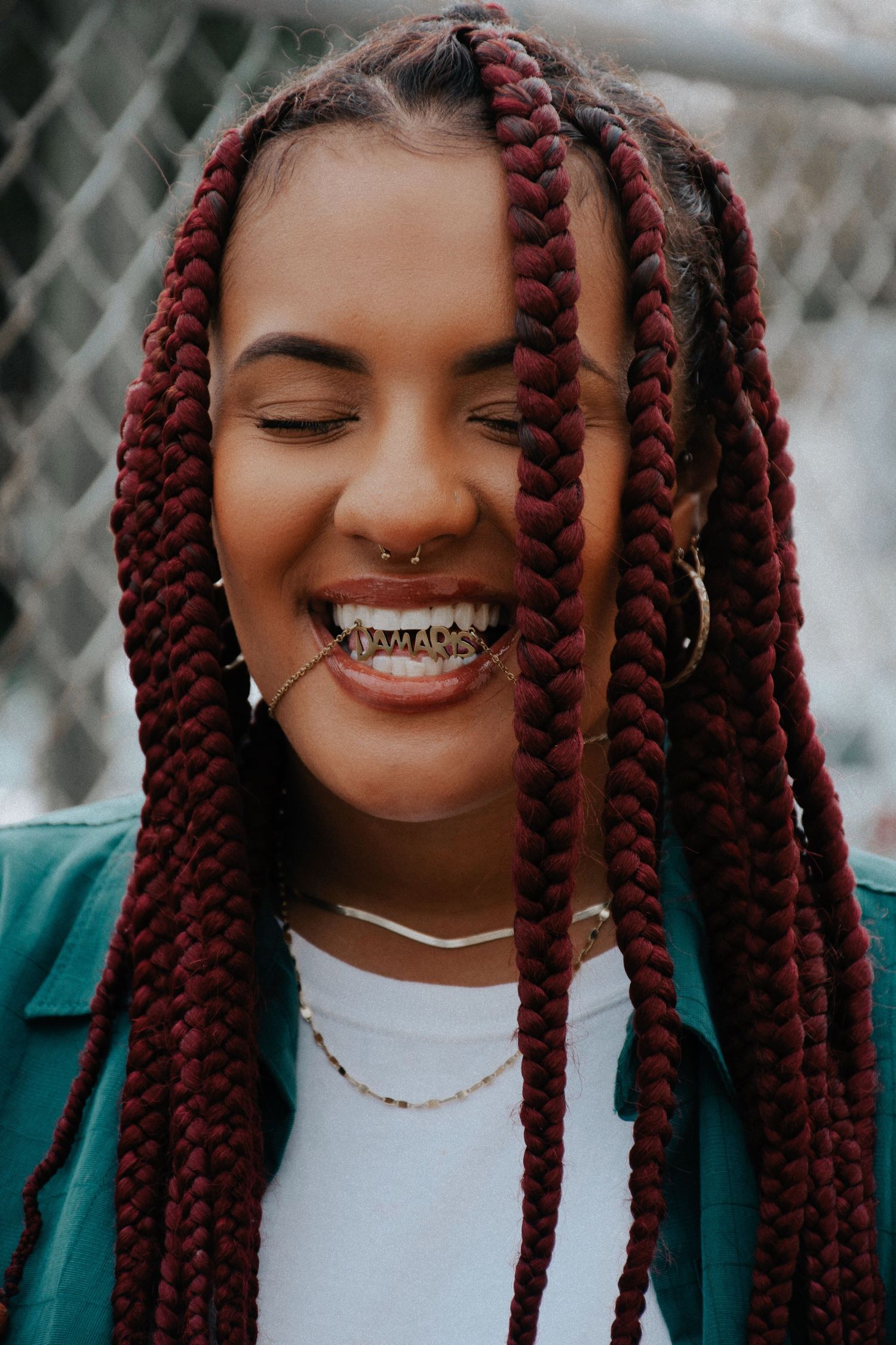 Close-up portrait showing burgundy braids and jewelry details against dark background.