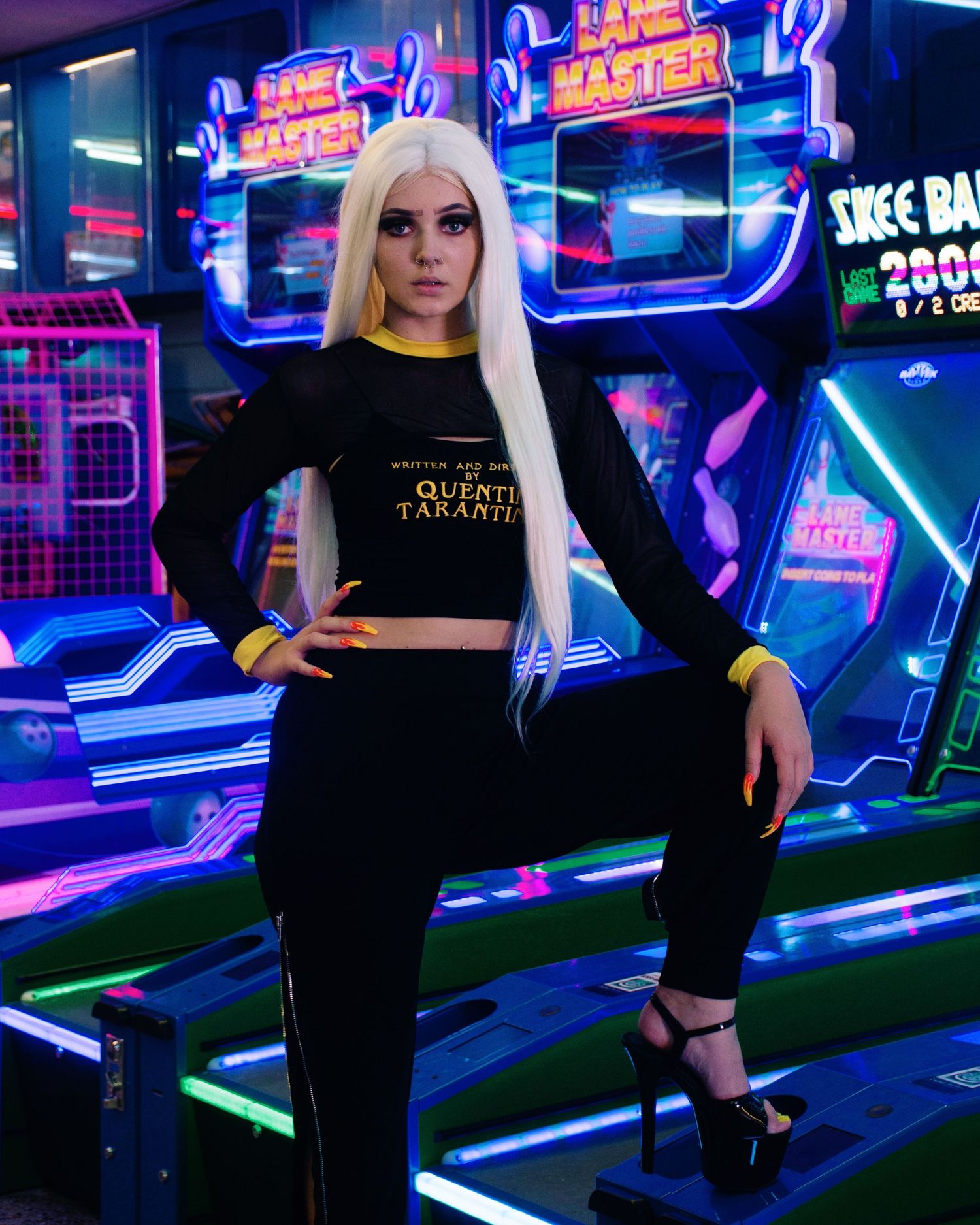 Edgy fashion shoot in neon-lit arcade with blue and purple lighting effects.