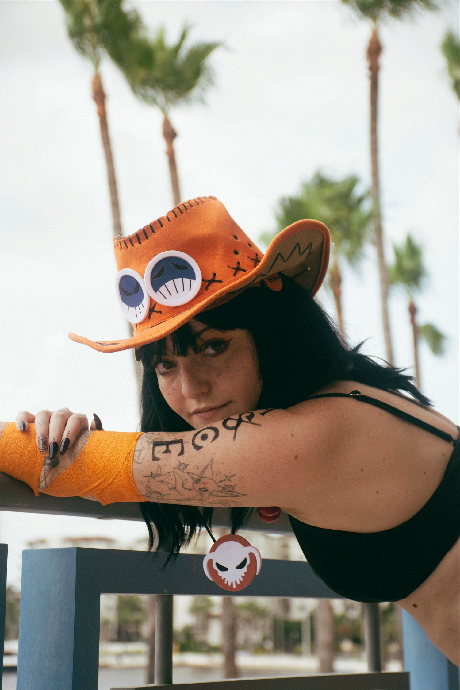 Cosplayer in orange cowboy hat and black outfit poses dramatically on railing.