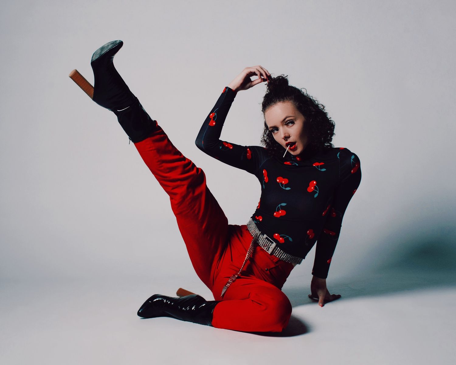 Dynamic fashion poses in red and black patterned outfit against studio backdrop.