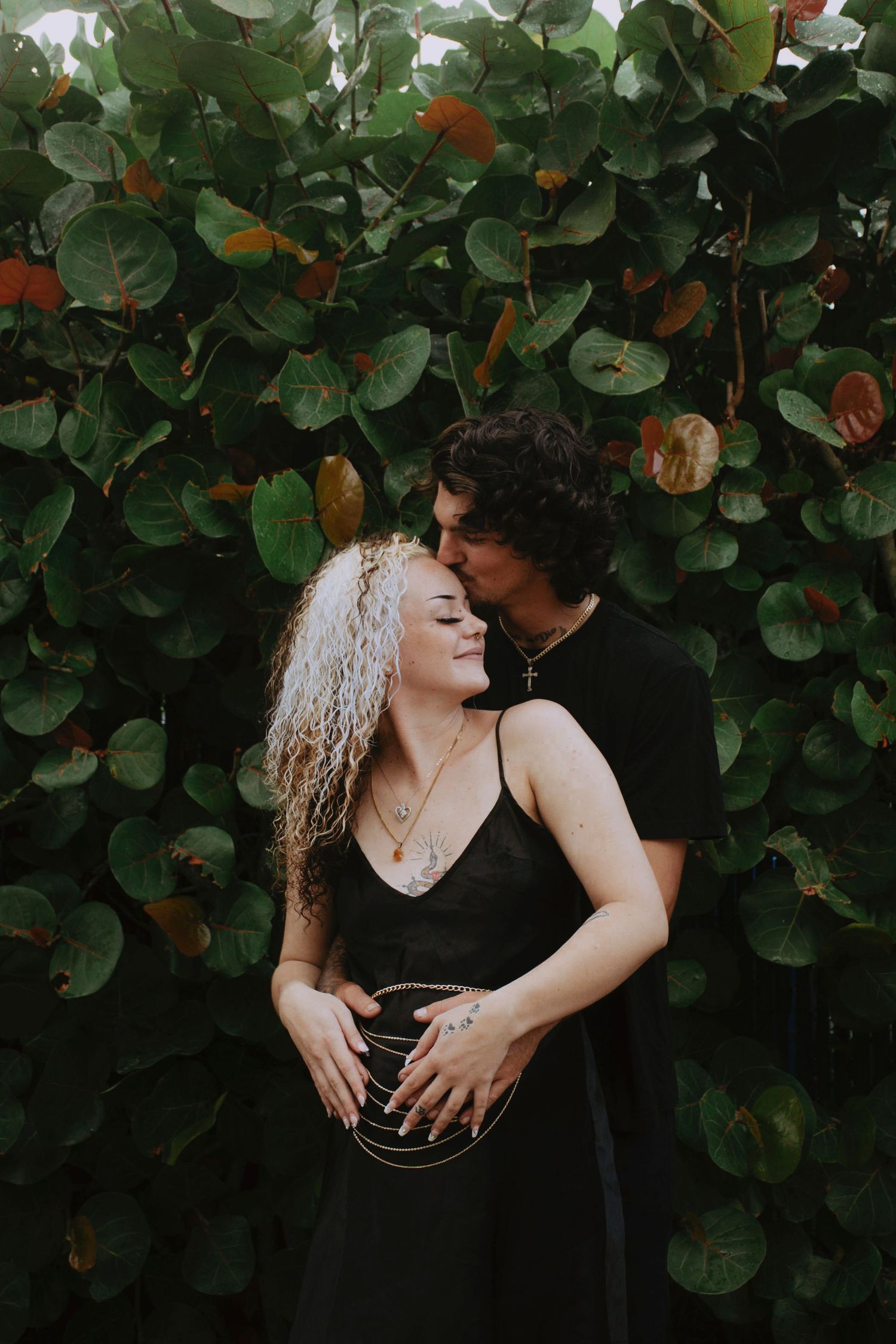 Romantic maternity photos of couple embracing against green foliage background.