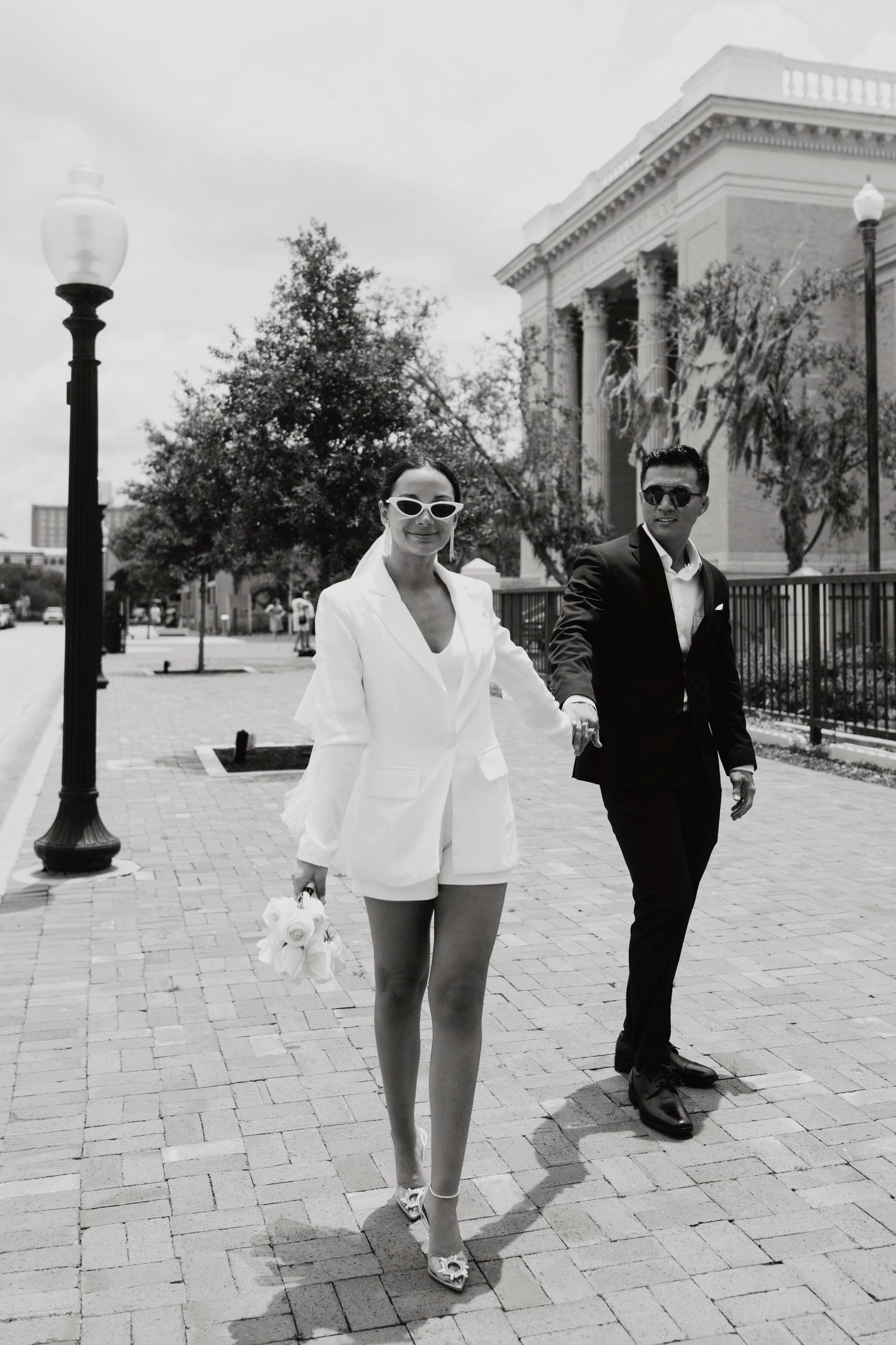 Elegant couple posing on white stone steps in formal attire with classical architecture in background.