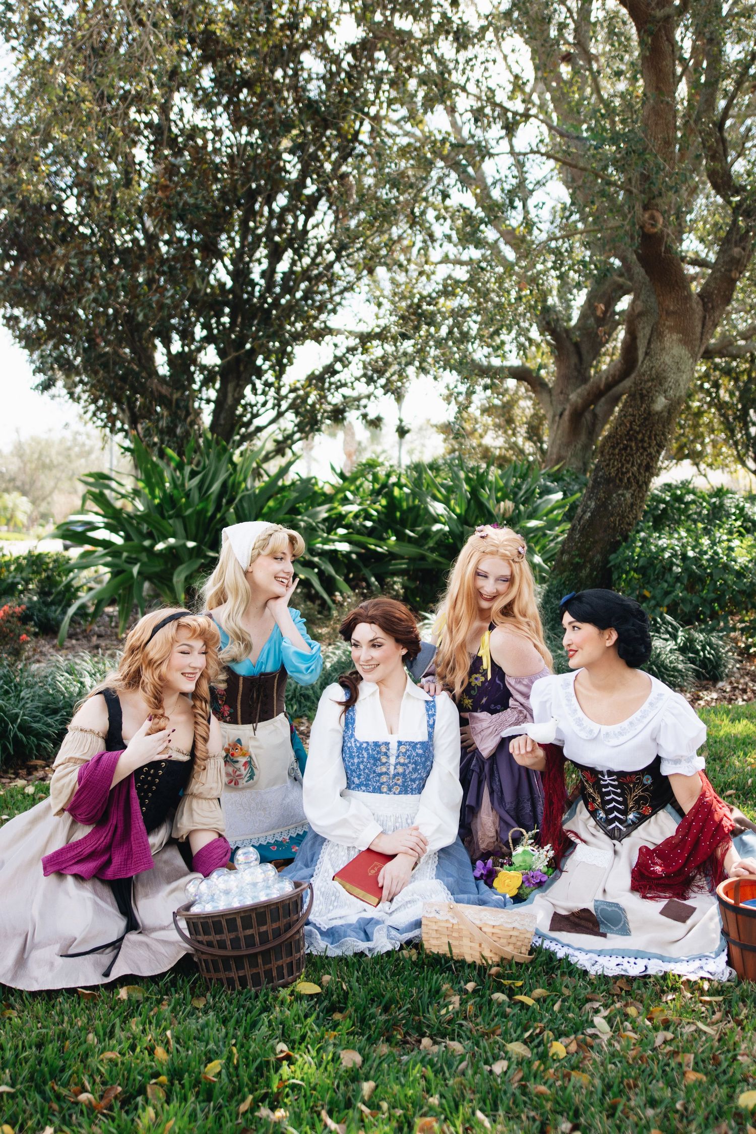 Group of friends in vintage costumes having a picnic under trees with baskets and blankets.