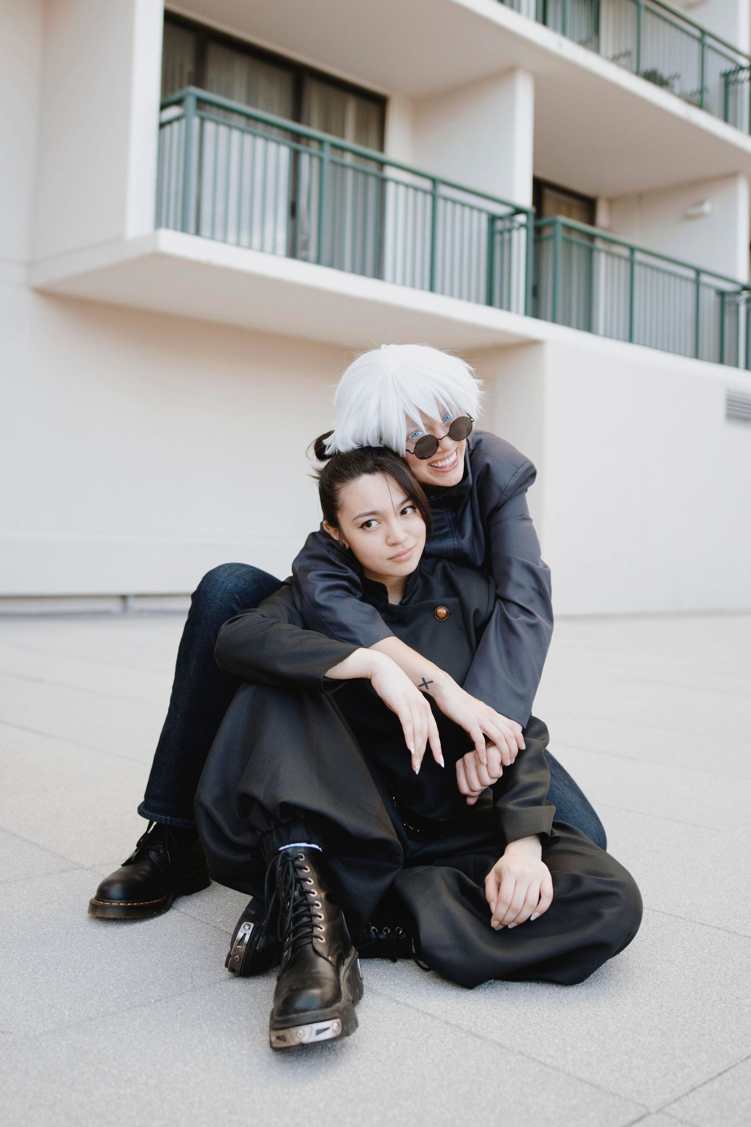 Two people in black outfits lounging on concrete urban setting.