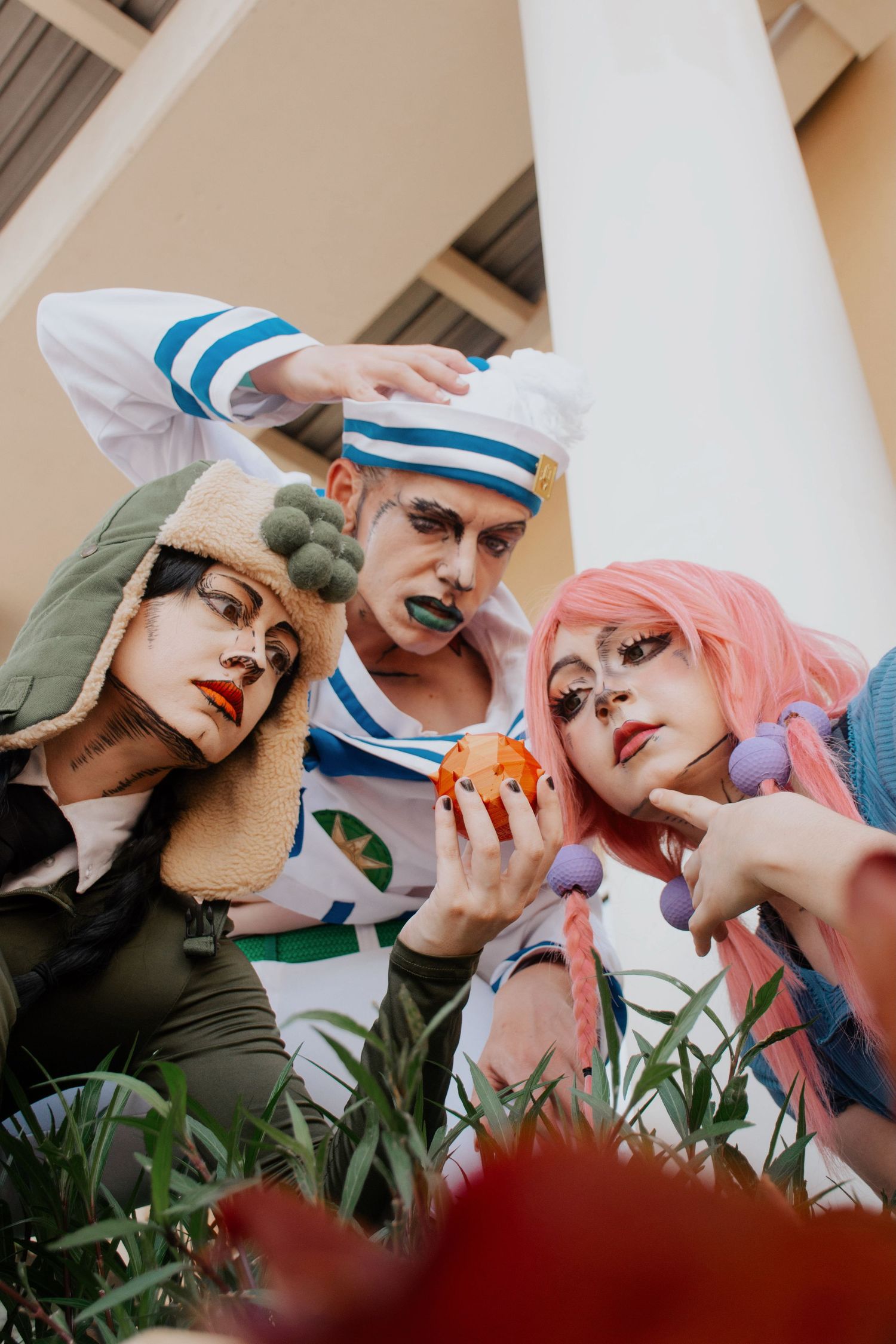 Group cosplay photo featuring three people in stylized makeup and costumes posing together.