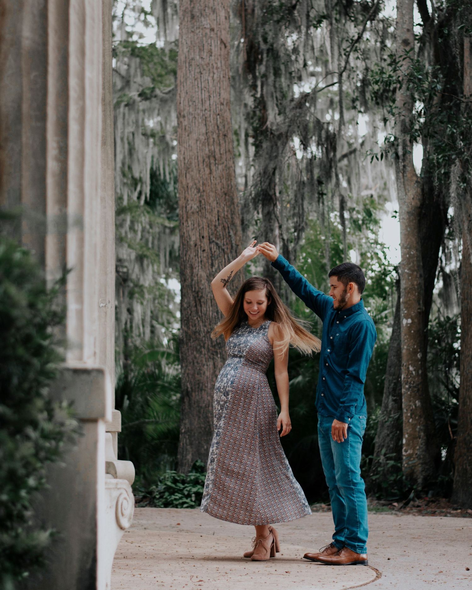 A playful couple dancing together between white columns in a park setting.