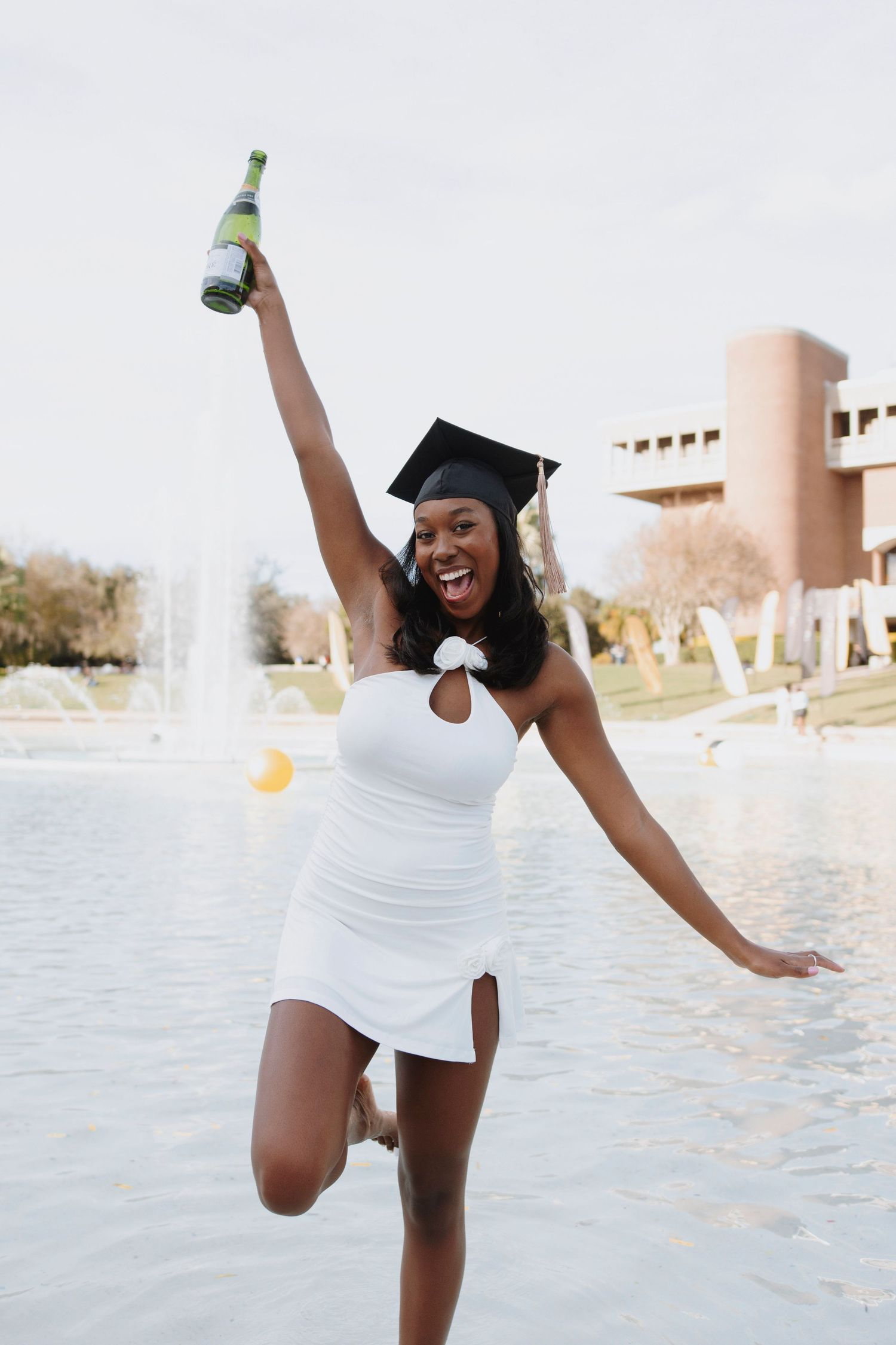 Graduation celebration photoshoot with champagne at campus fountain.