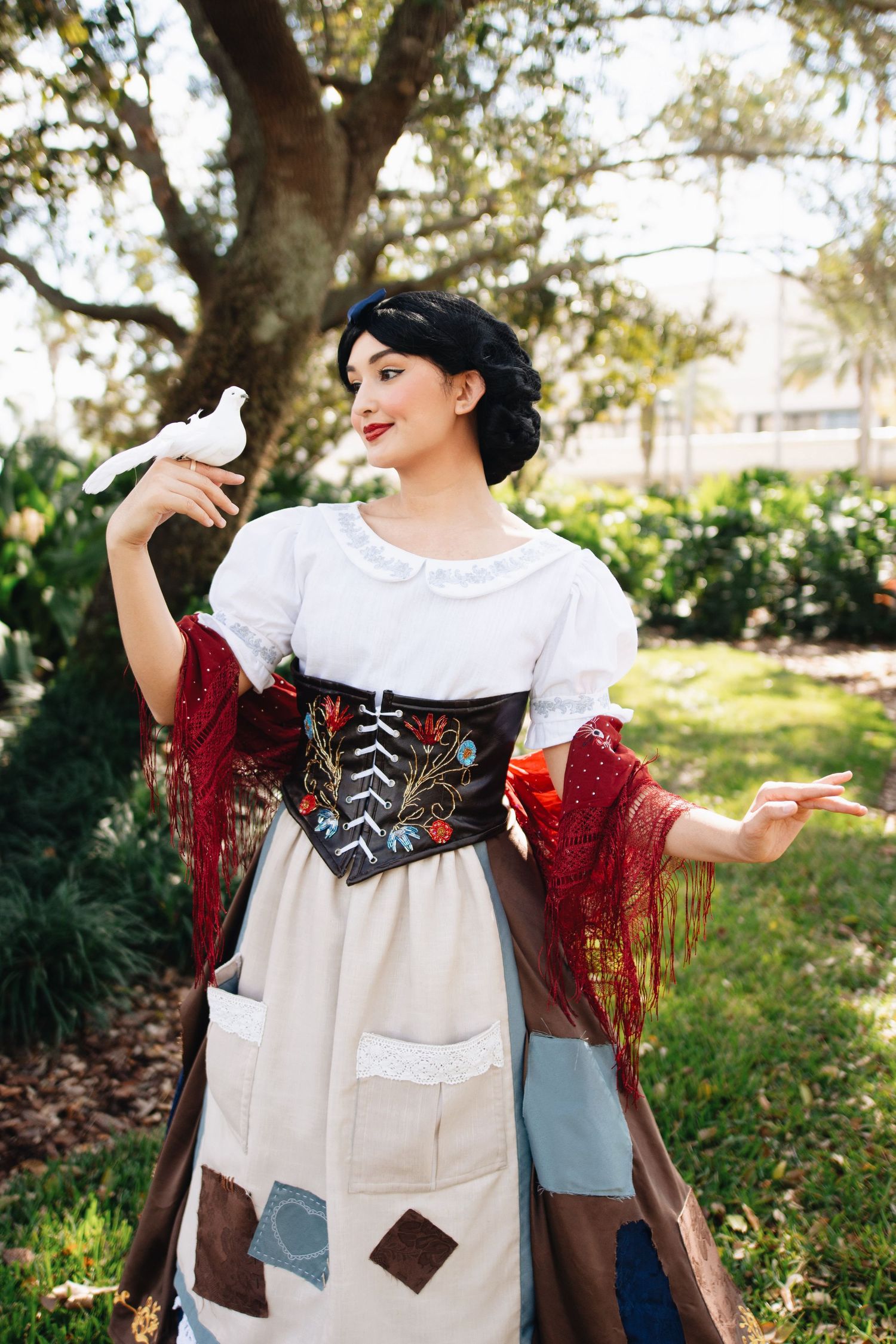 A peasant-style costume with white blouse, embroidered corset, and patchwork skirt in an outdoor setting.