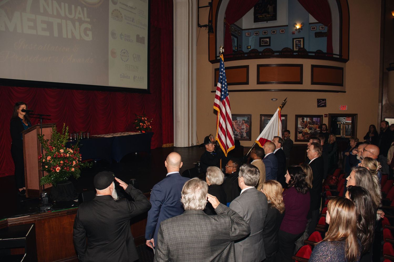 A group of people stand and raise their hands during what appears to be a political or community gathering.