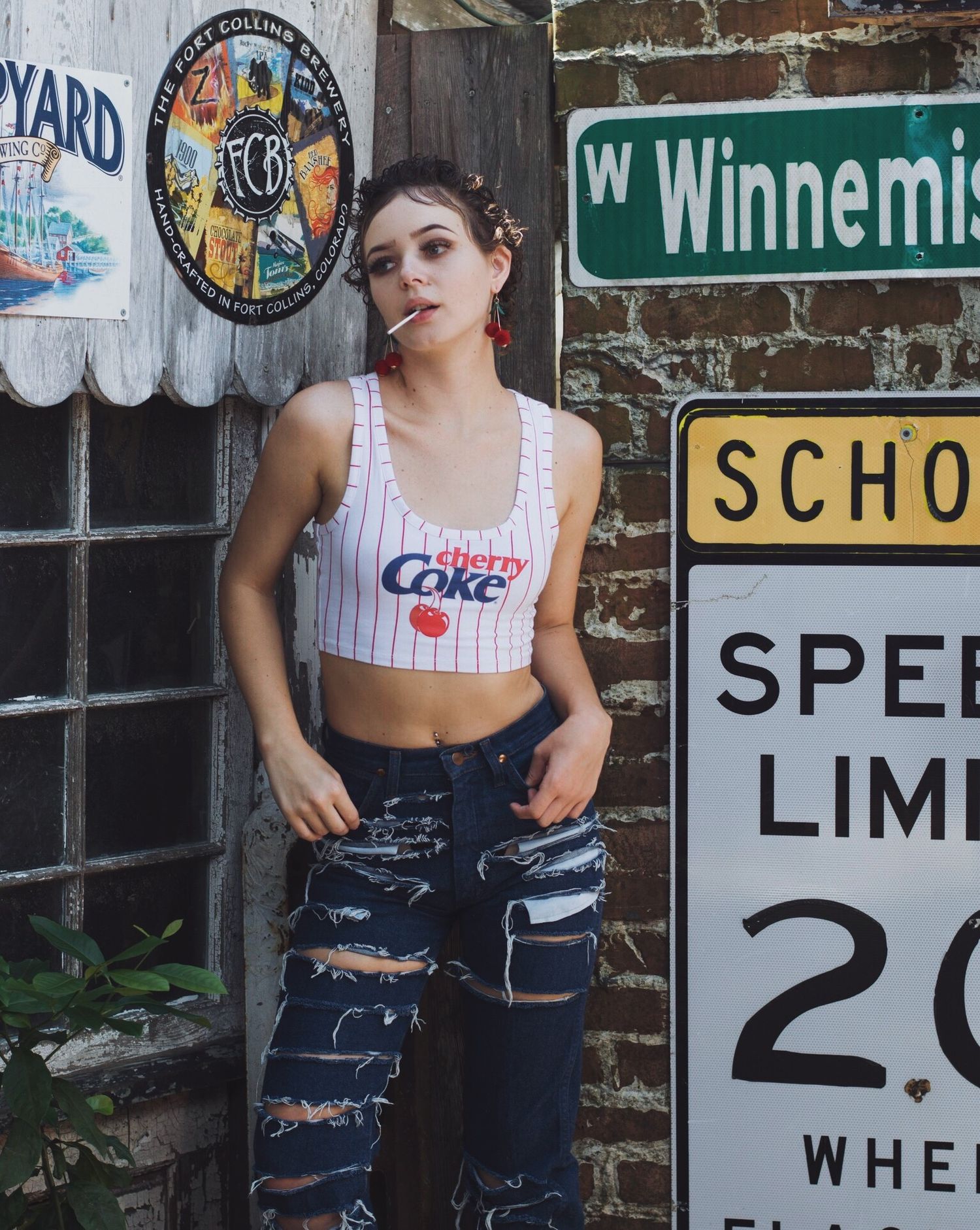 Street style photos against brick wall with vintage signs featuring casual denim and tank top look.