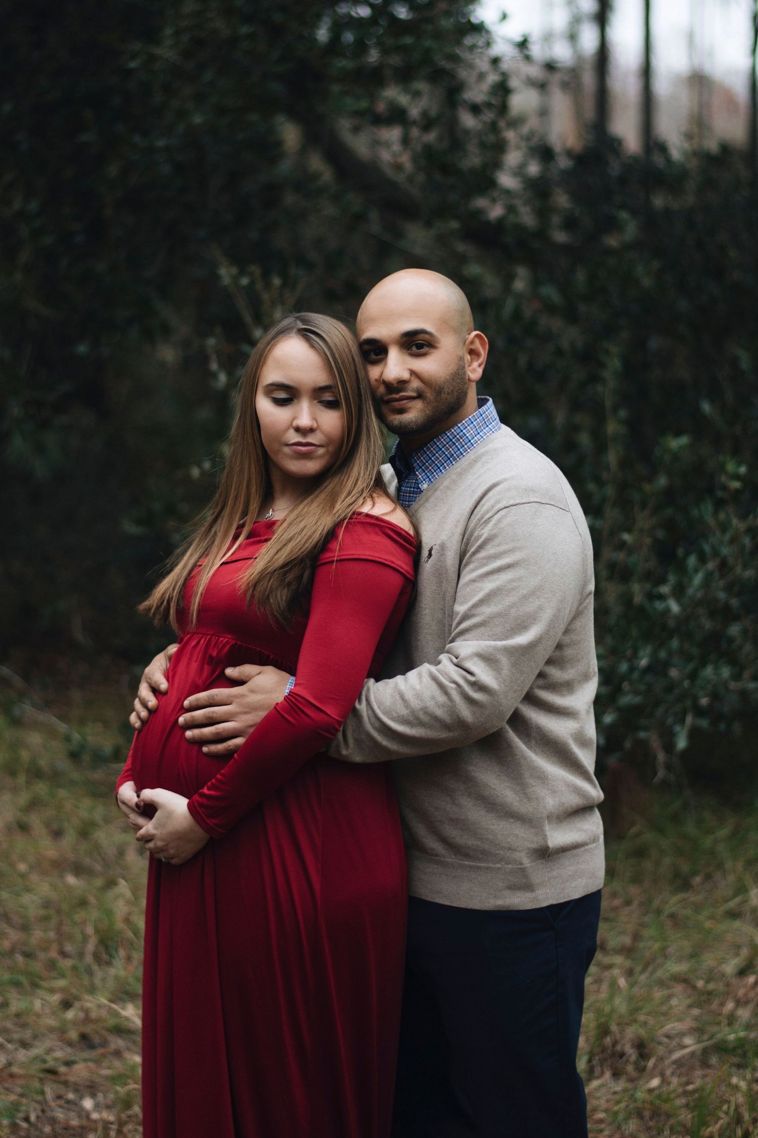 A couple embraces during their maternity session wearing burgundy and beige.