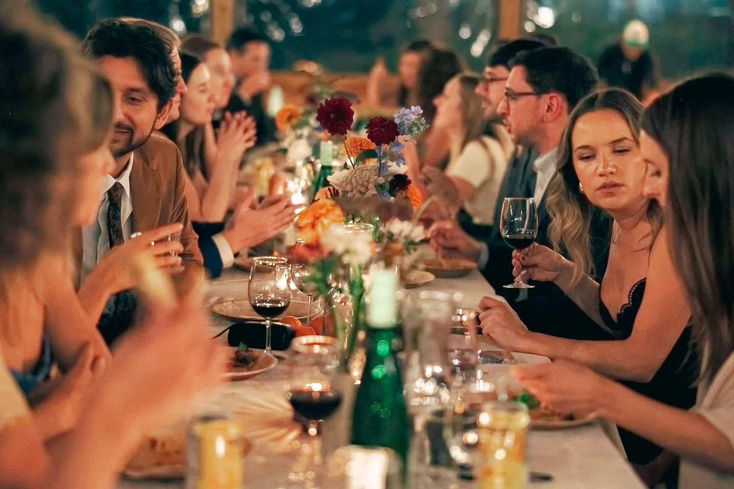 Candlelit dinner party wedding with guests enjoying wine and conversation at a long table in a dimly lit restaurant, micro wedding in NC tip
