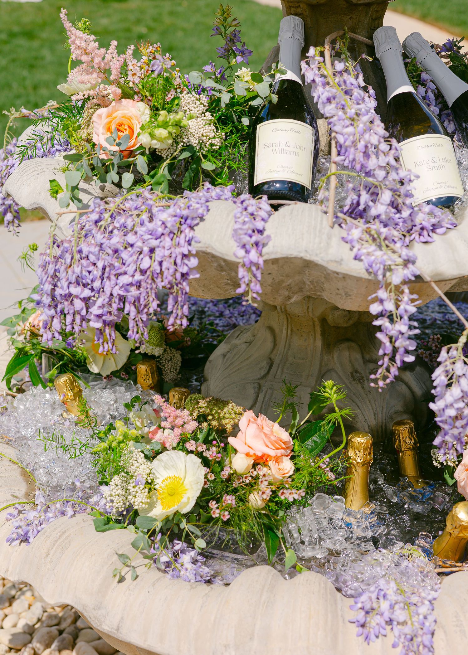 Microwedding photos elegant outdoor party setup with cascading wisteria flowers champagne bottles, and peach roses on a rustic wooden table.
