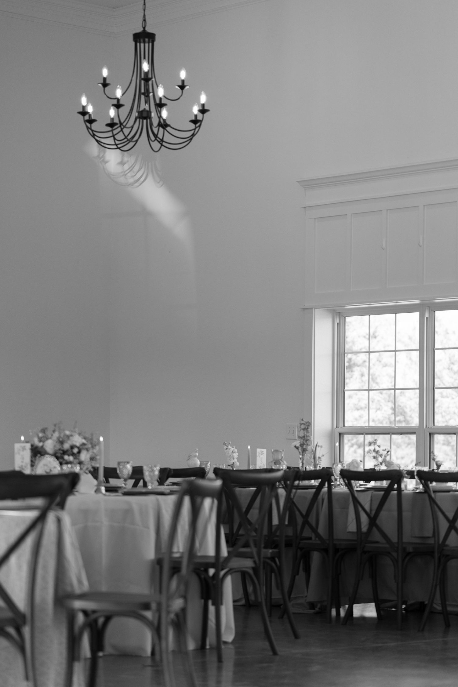 A series of elegant dining tables with white tablecloths and black chairs arranged in a bright room with chandeliers, micro wedding in NC