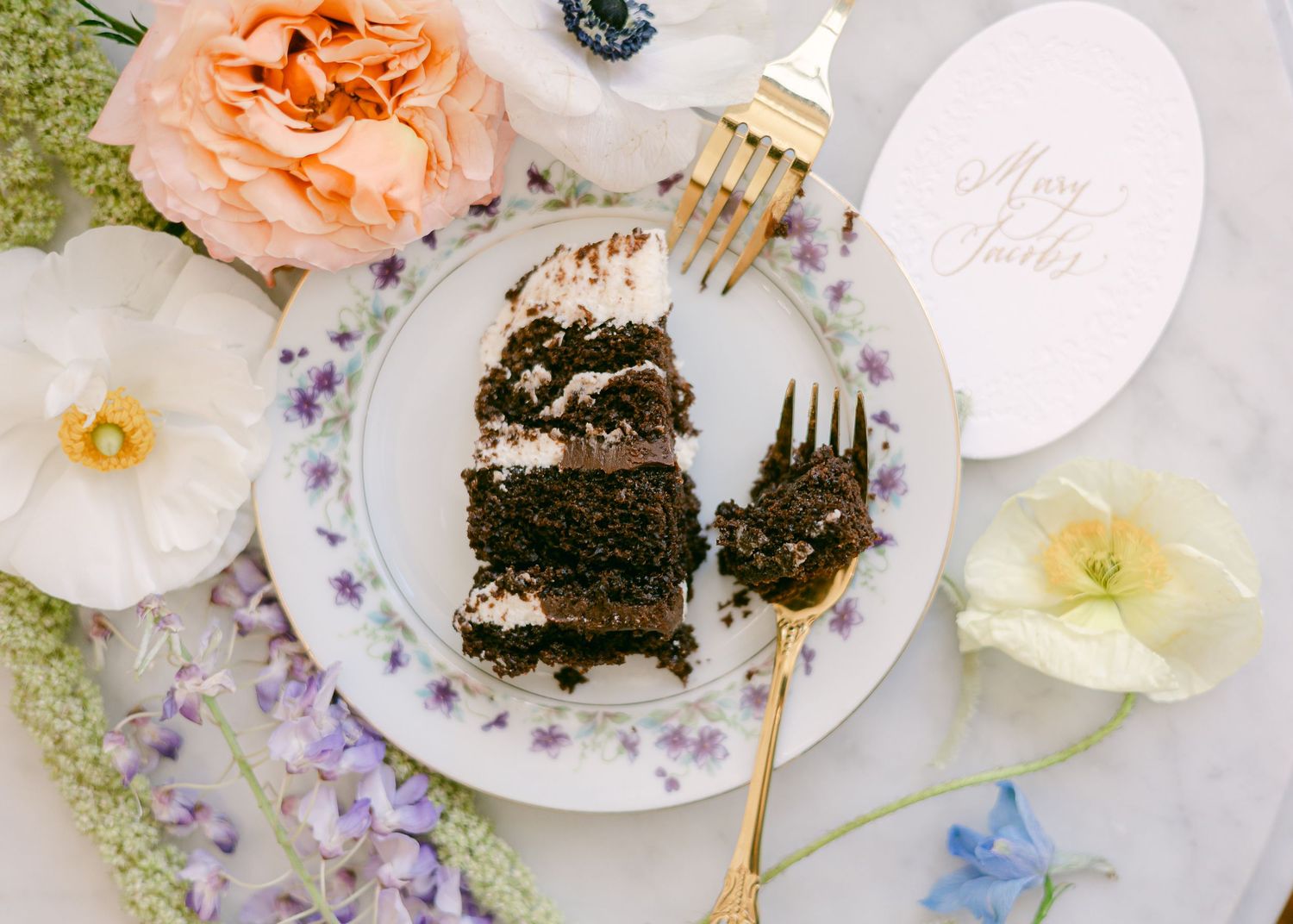 Microwedding photos Elegant table setting with slices of chocolate cake, delicate floral plates, and soft peach roses on a white tablecloth.