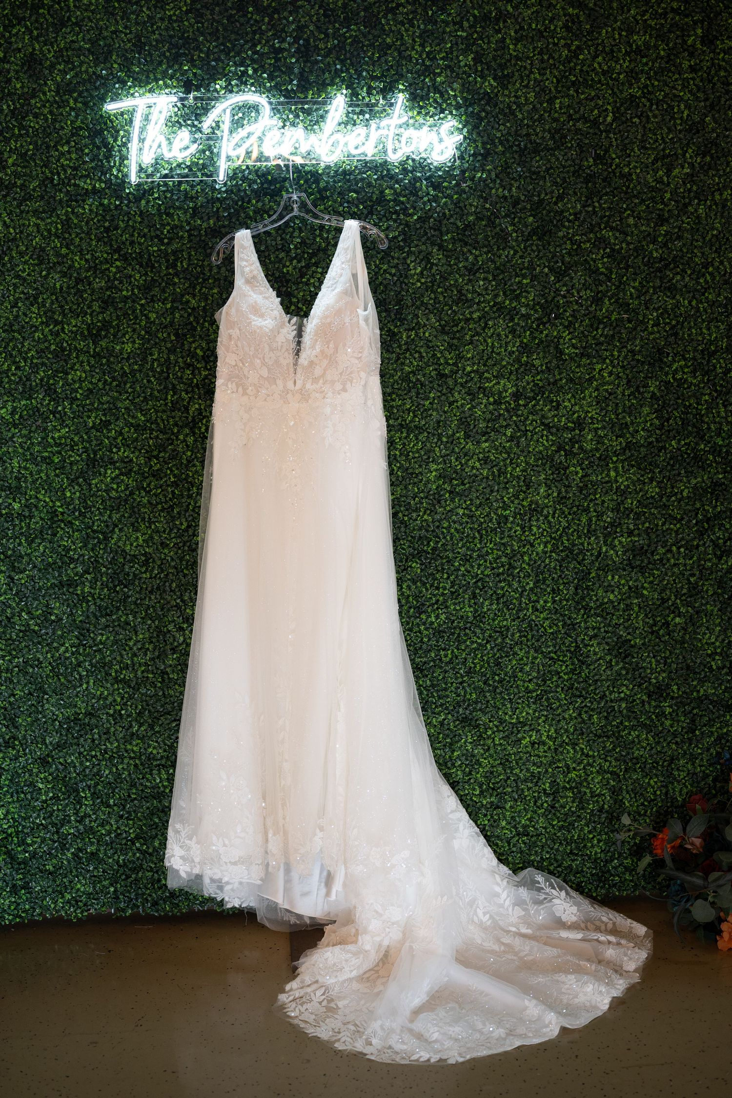 Wedding dress display against green hedge wall with illuminated neon signage.