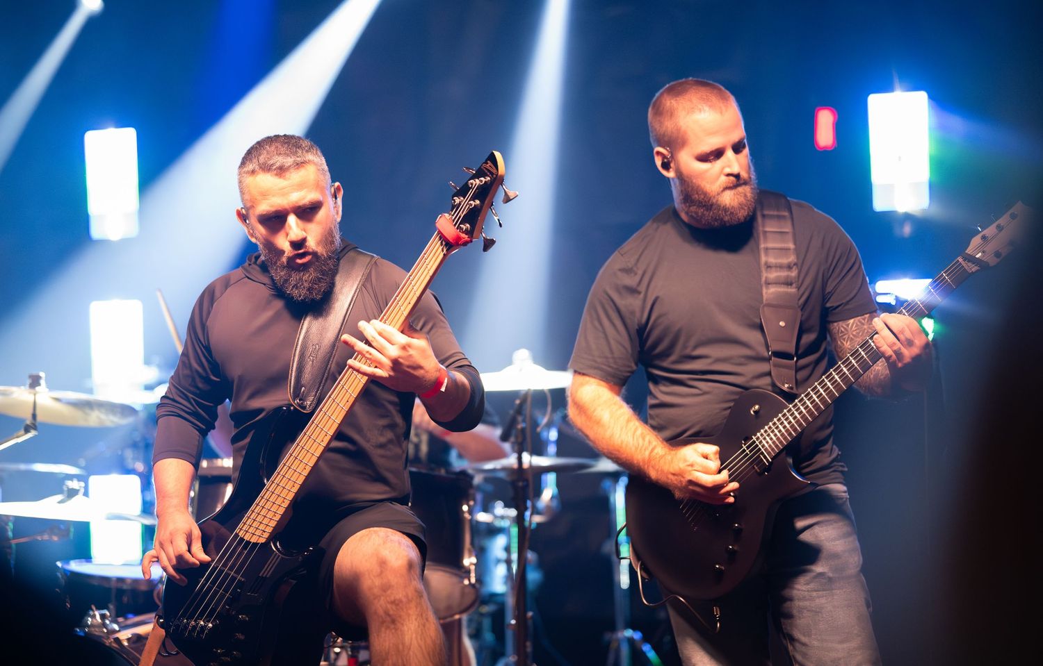 Musicians play guitars during an energetic performance with blue stage lighting effects.