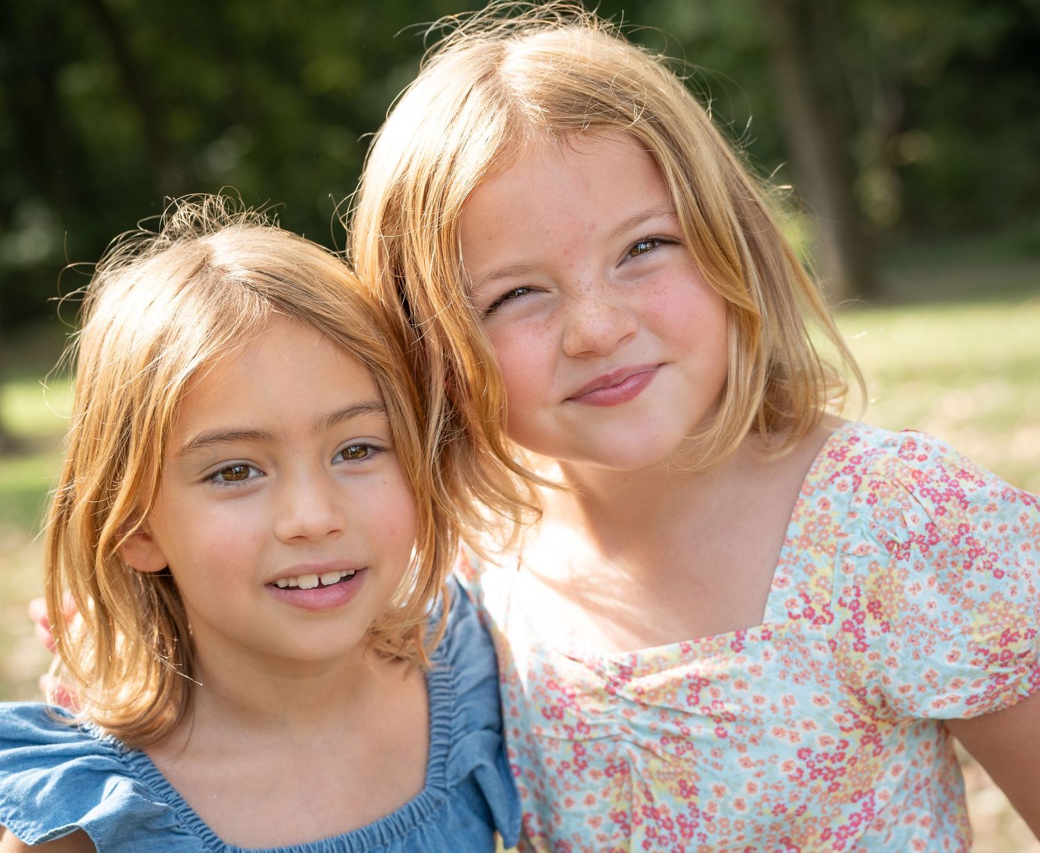 Two children with blonde hair share a playful moment outdoors in natural lighting.