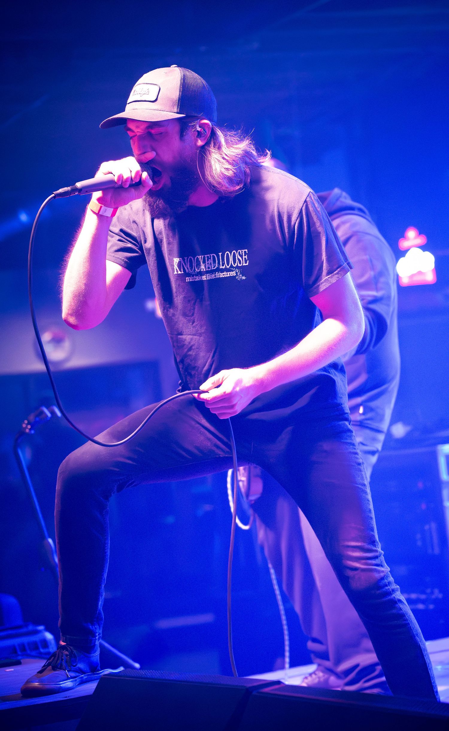 Performer in casual attire singing passionately under blue stage lights at music venue.