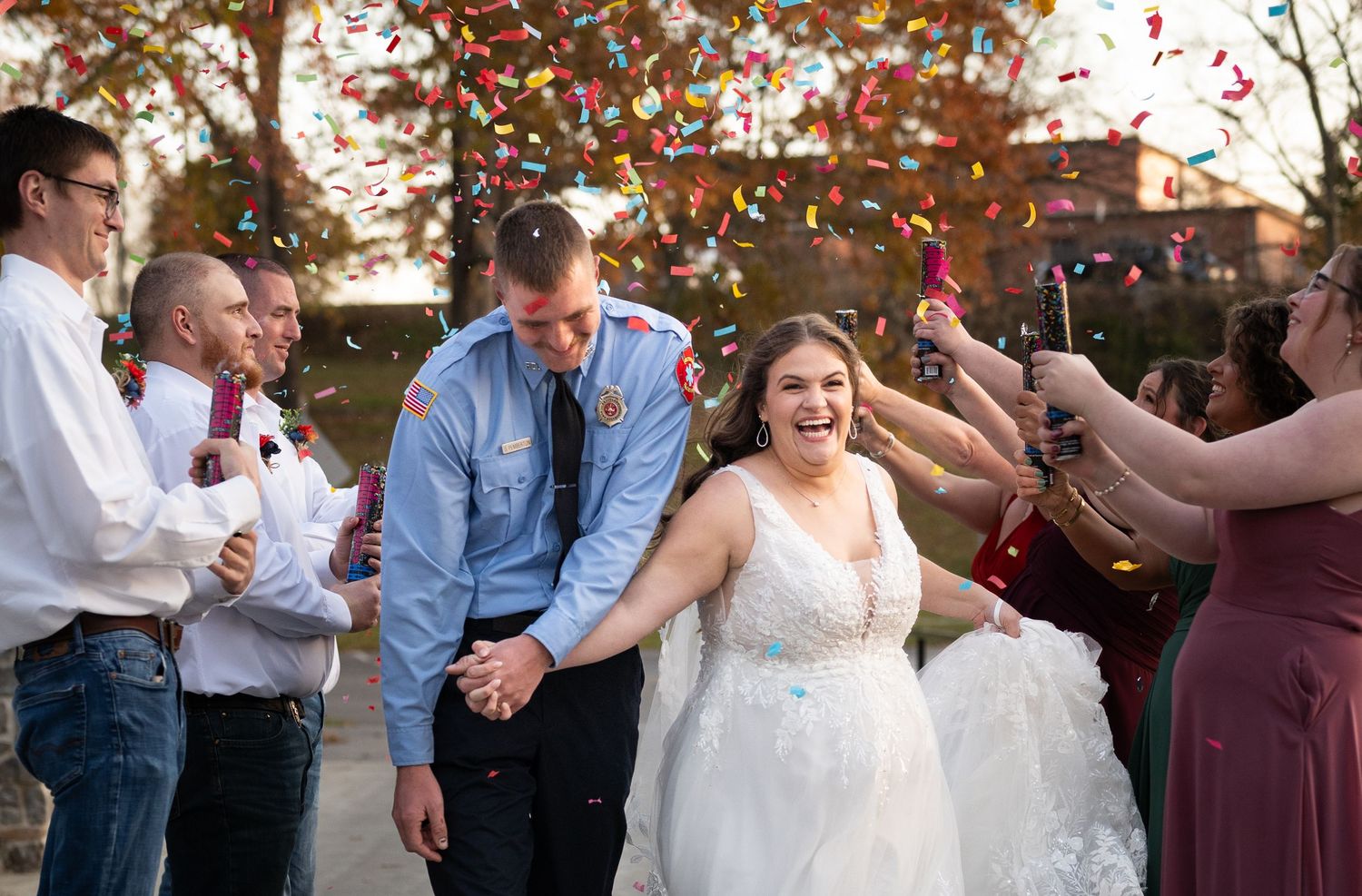 Wedding guests throw red rose petals during an outdoor celebration at sunset.
