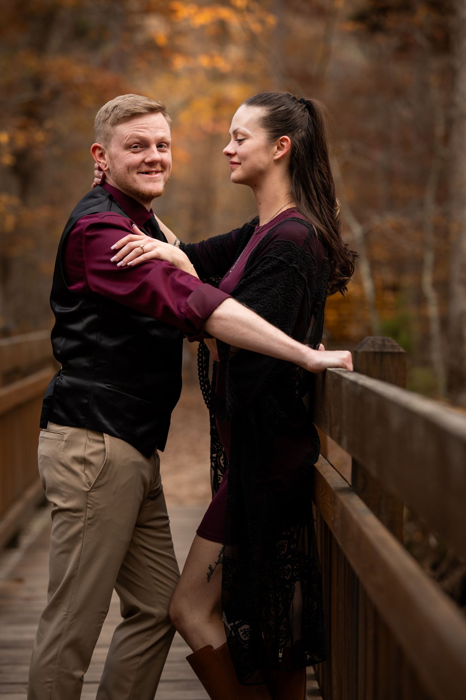 A couple shares a romantic moment on a wooden bridge surrounded by autumn foliage.