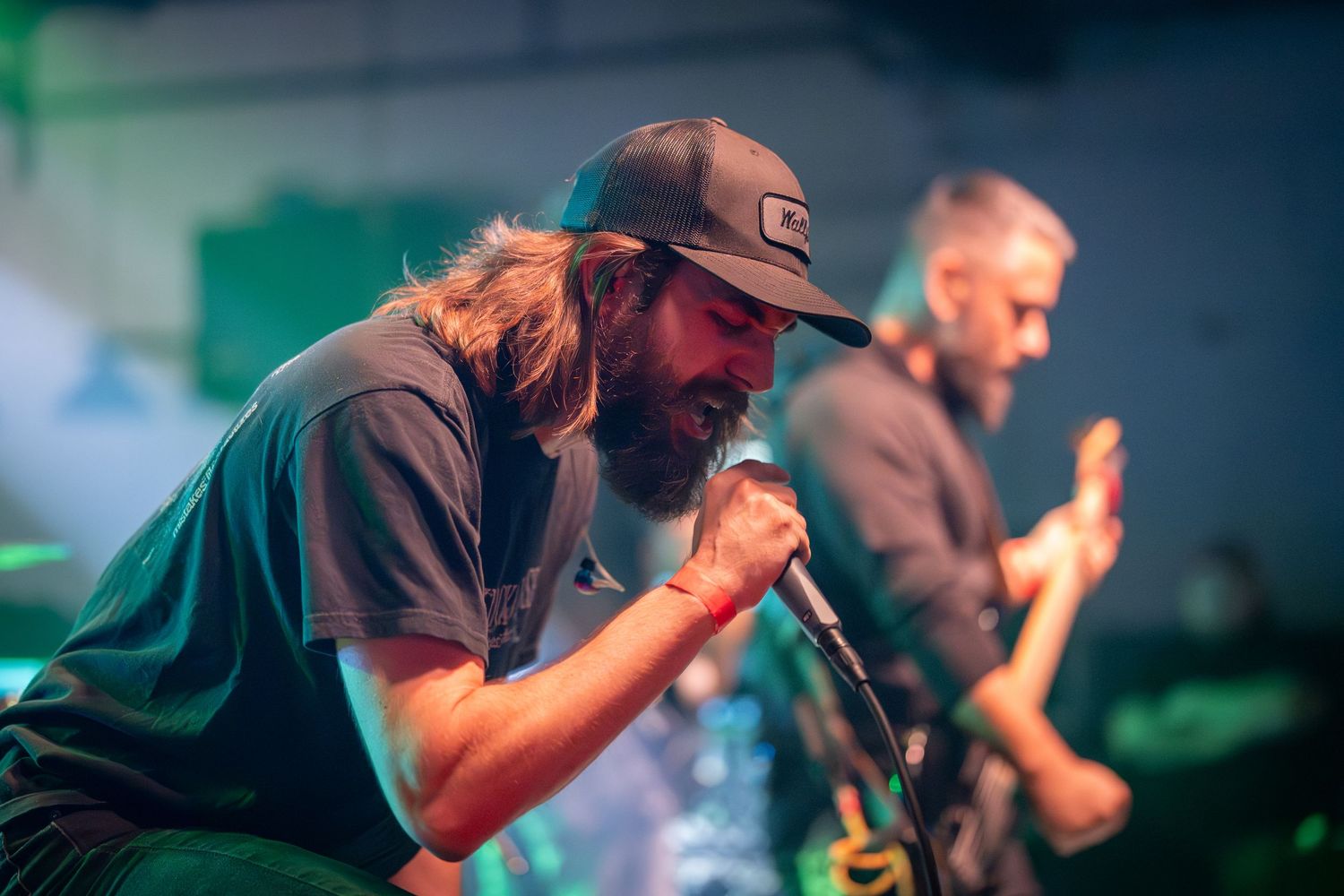 Rock band performs energetically on stage with dramatic green lighting and fog effects during live concert.