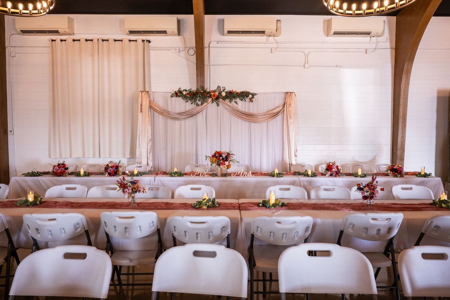 Wedding reception venue with rows of tables and chairs set up under crystal chandeliers.