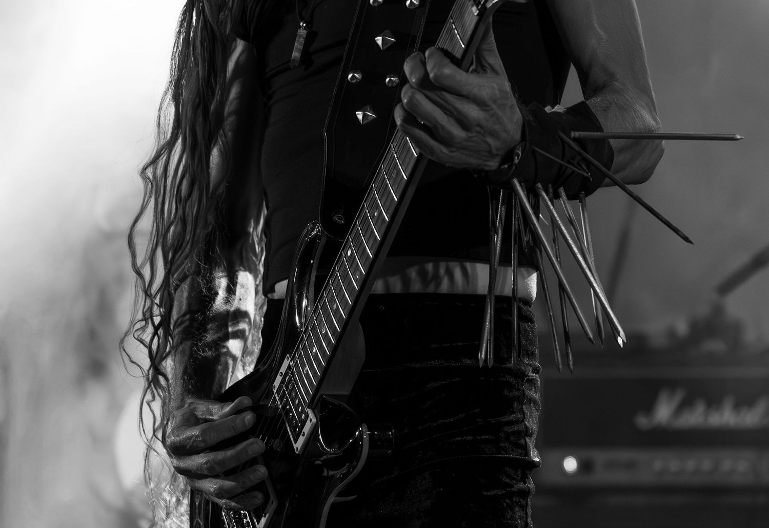 A black and white photo shows a guitarist performing on stage with long hair and an electric guitar.