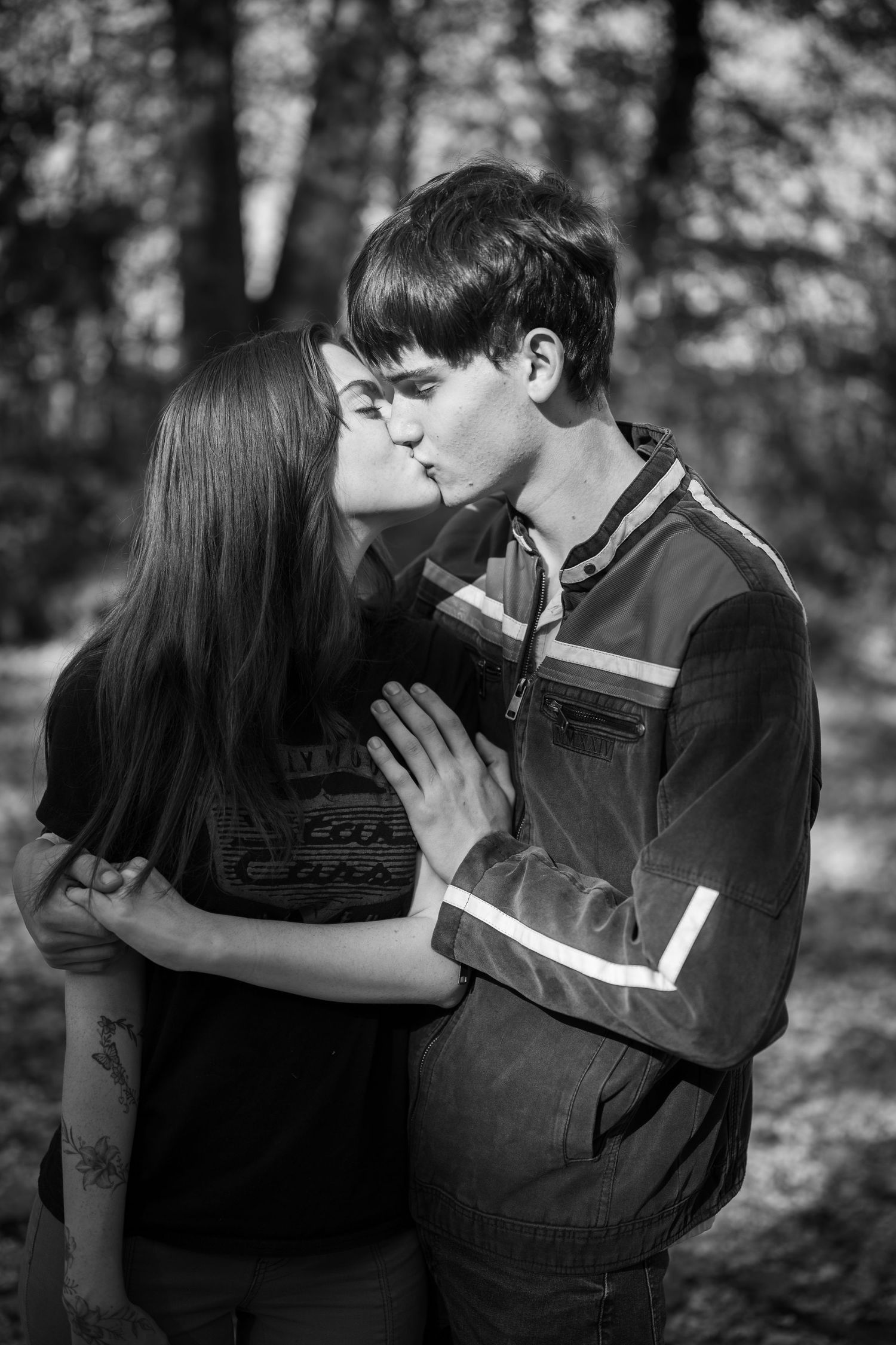 A romantic black and white photo of a couple sharing a tender kiss in a forest setting.