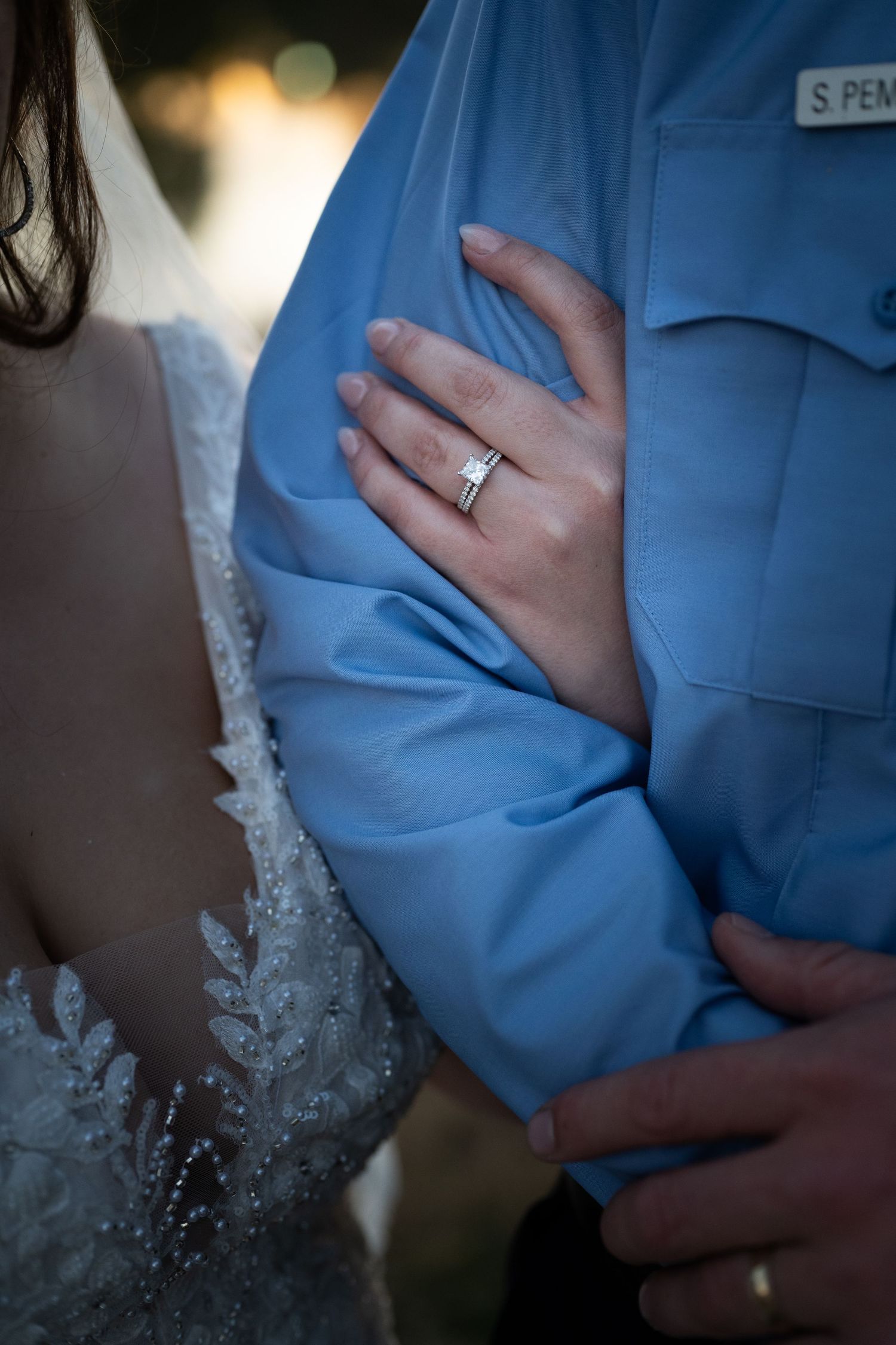 Close-up of hands showing wedding rings against blue formal attire and white lace dress.