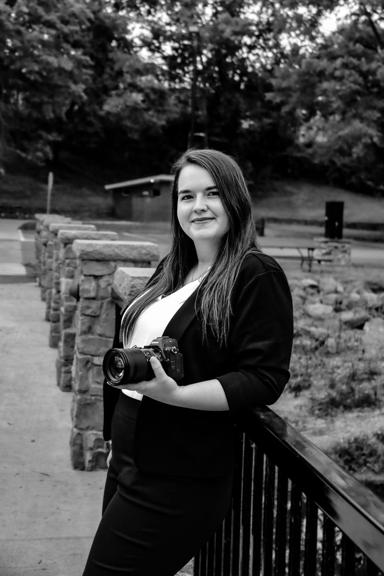 A person in black clothing sits on a wooden bench in an outdoor park setting with stone columns visible in background.