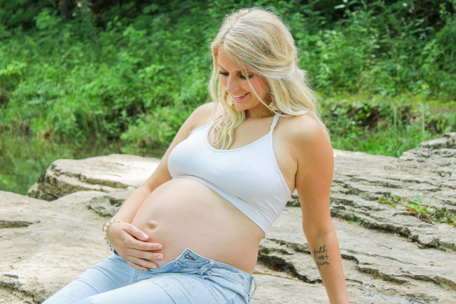 An expectant mother in casual attire rests on rocky terrain during a maternity photoshoot.