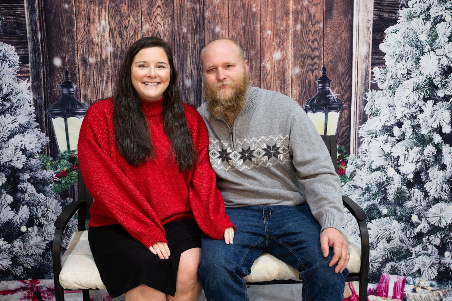 Couple poses together in front of snowy winter Christmas trees and decorations in a holiday photo session.