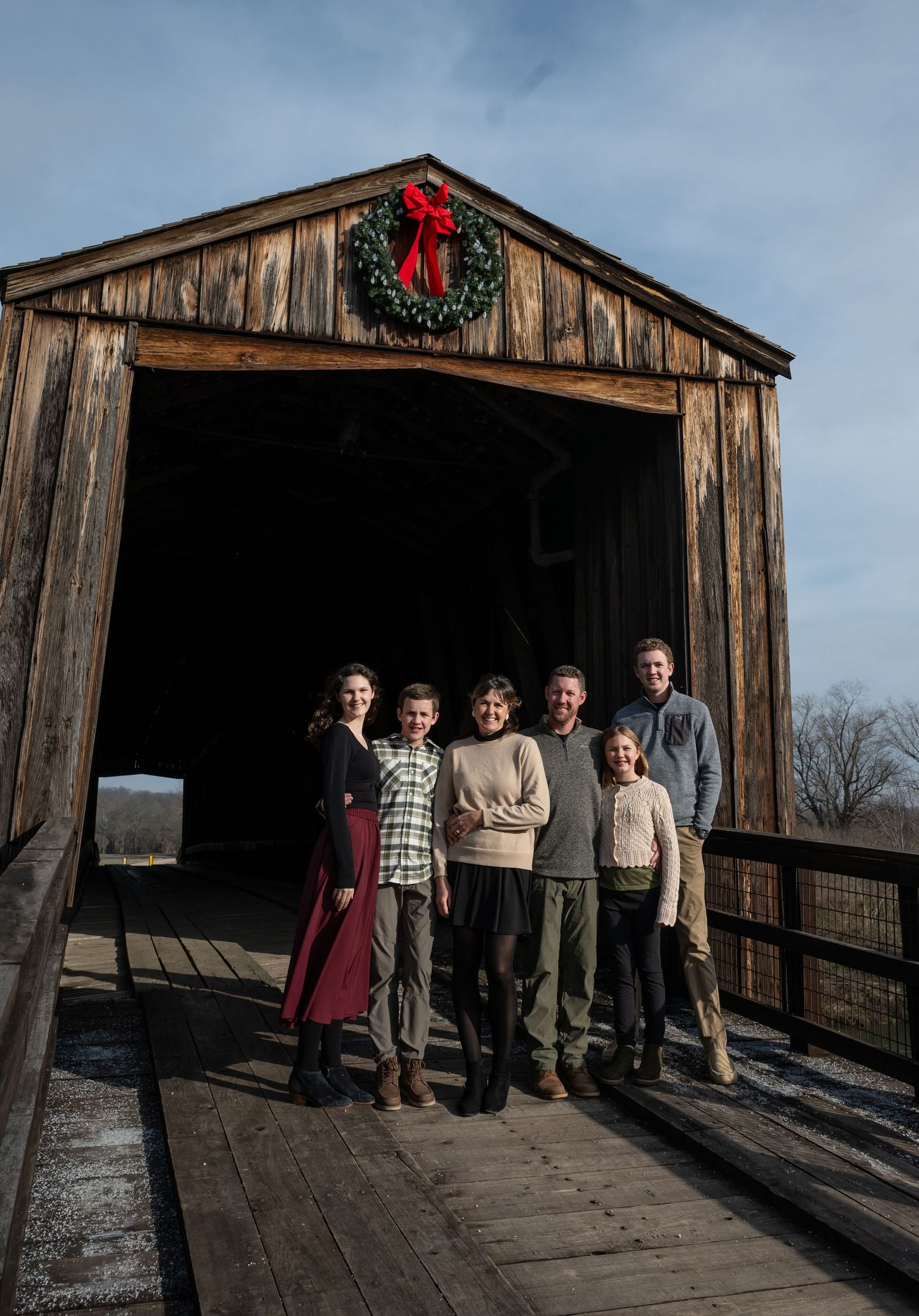 Group photo in front of rustic wooden barn with Christmas wreath.