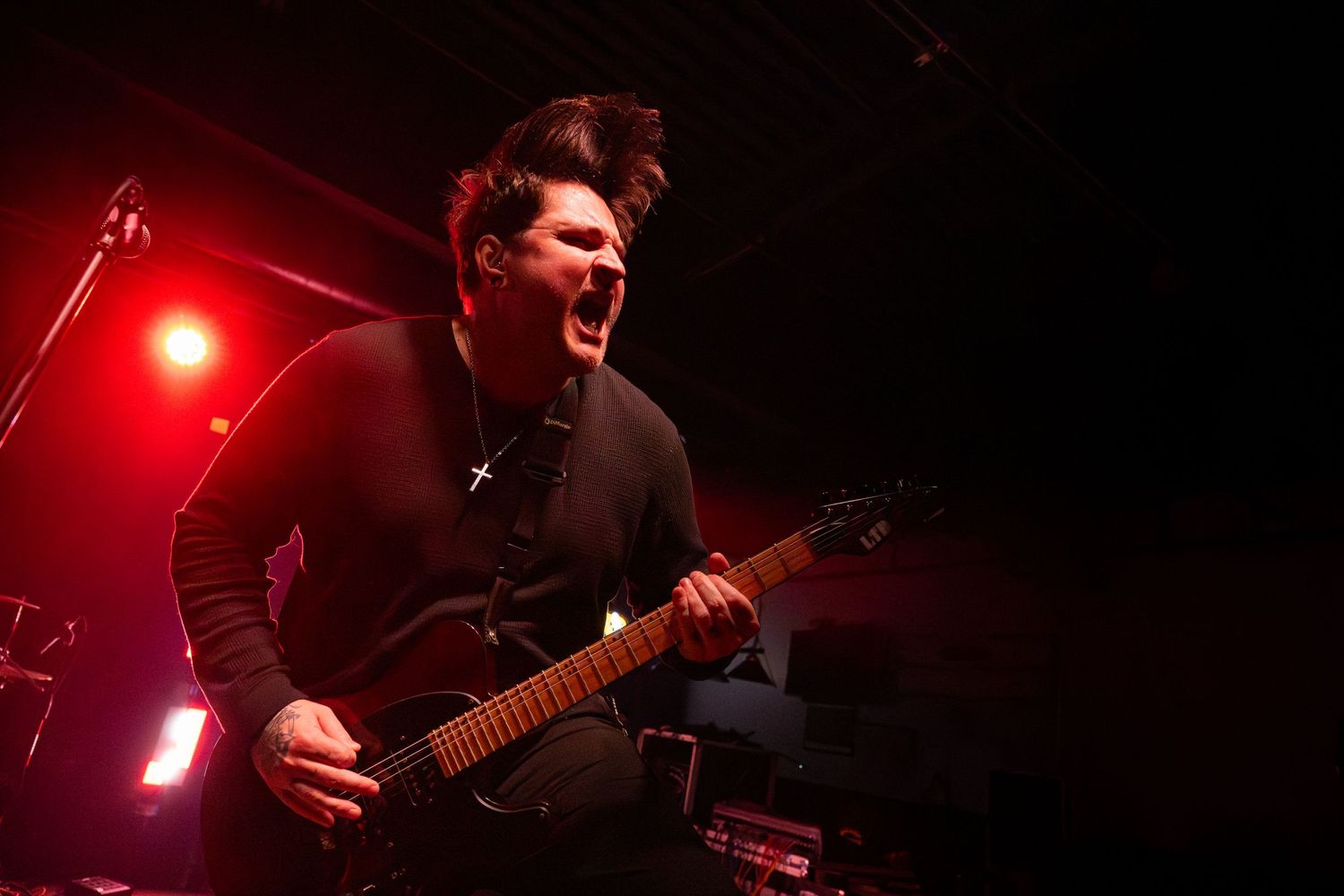 Musician performing with guitar under intense red stage lighting at live concert venue.