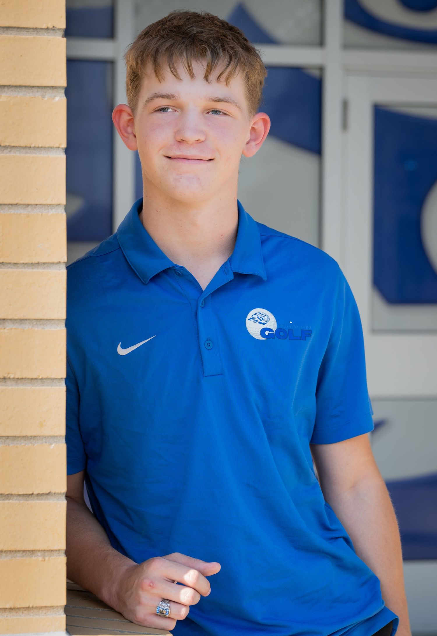 Student in royal blue Nike polo shirt poses against beige column background at school.