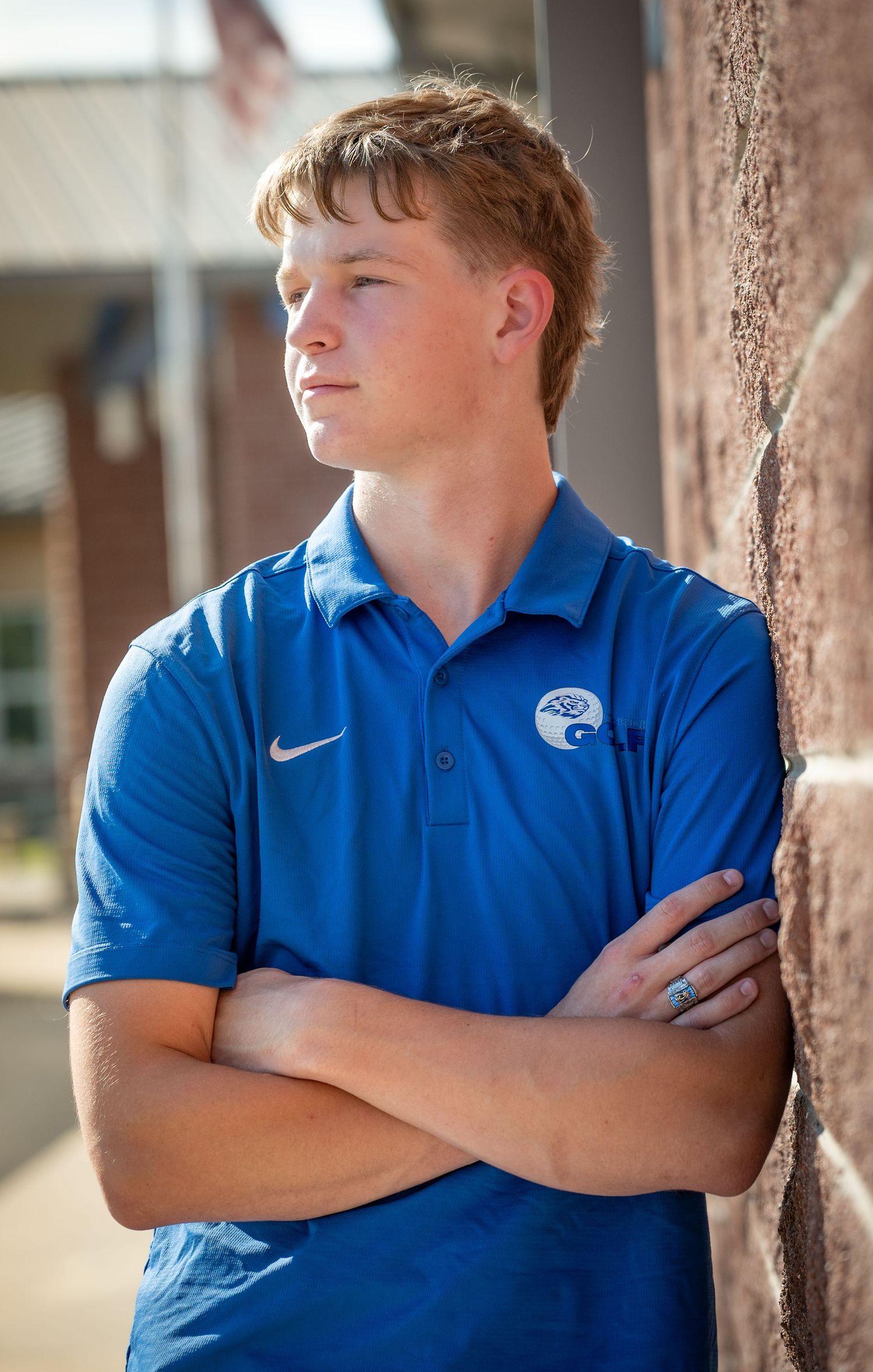 A student in a blue polo shirt stands against a brick wall with arms crossed in multiple poses.