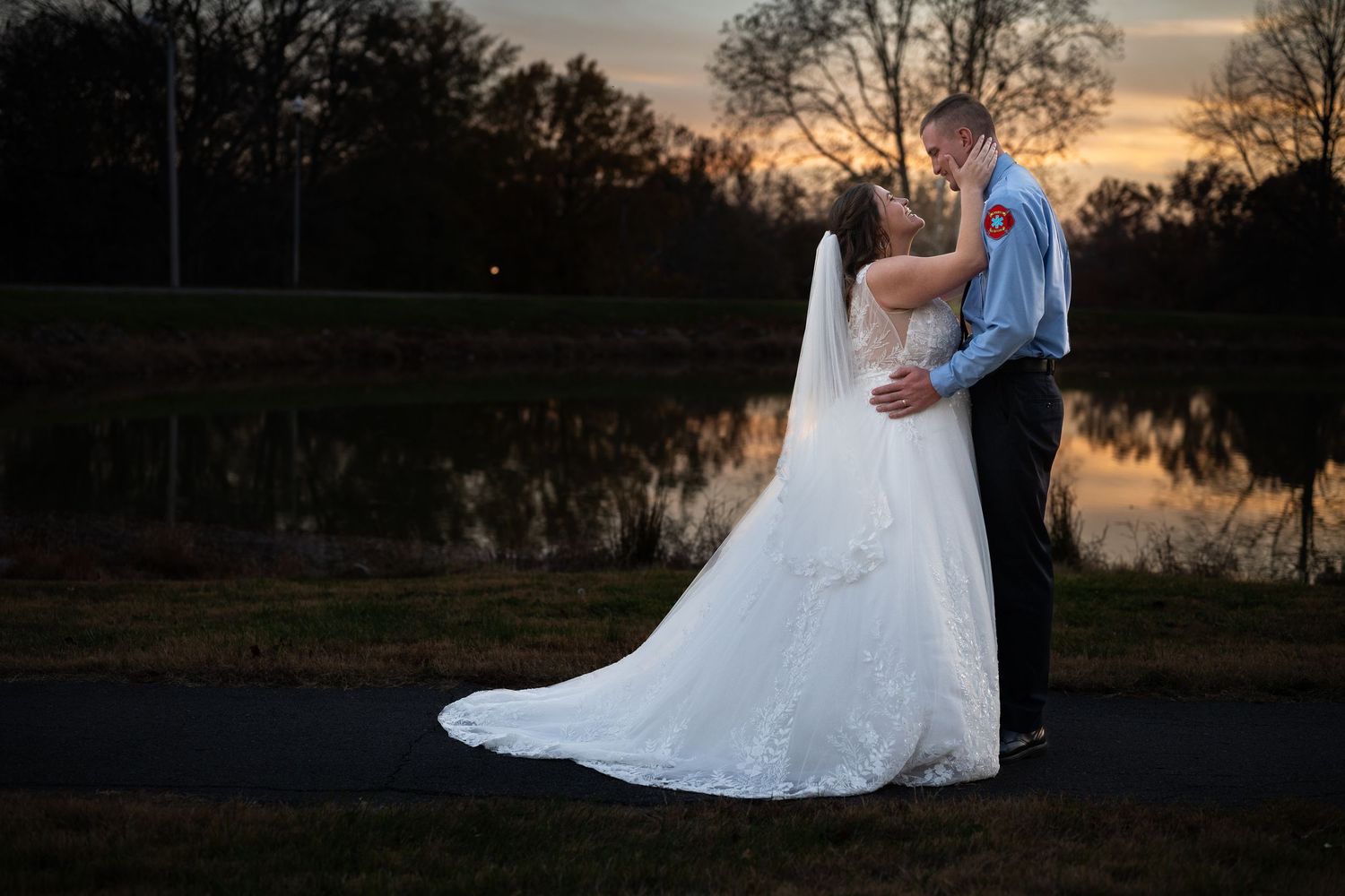 Silhouettes of wedding couple dancing against a golden sunset by a lake.