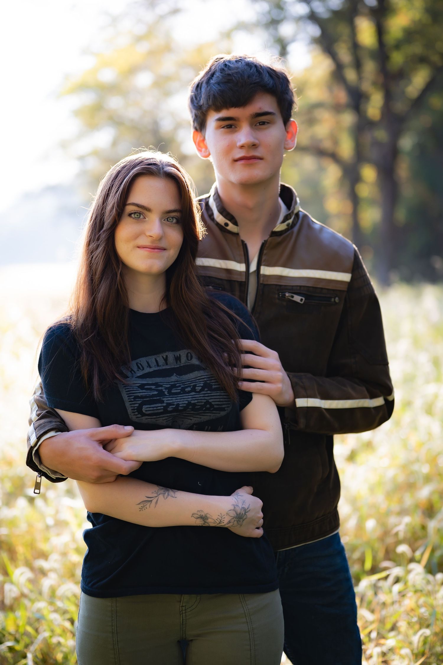 A couple embraces outdoors in sunlit field with wildflowers and natural bokeh background.
