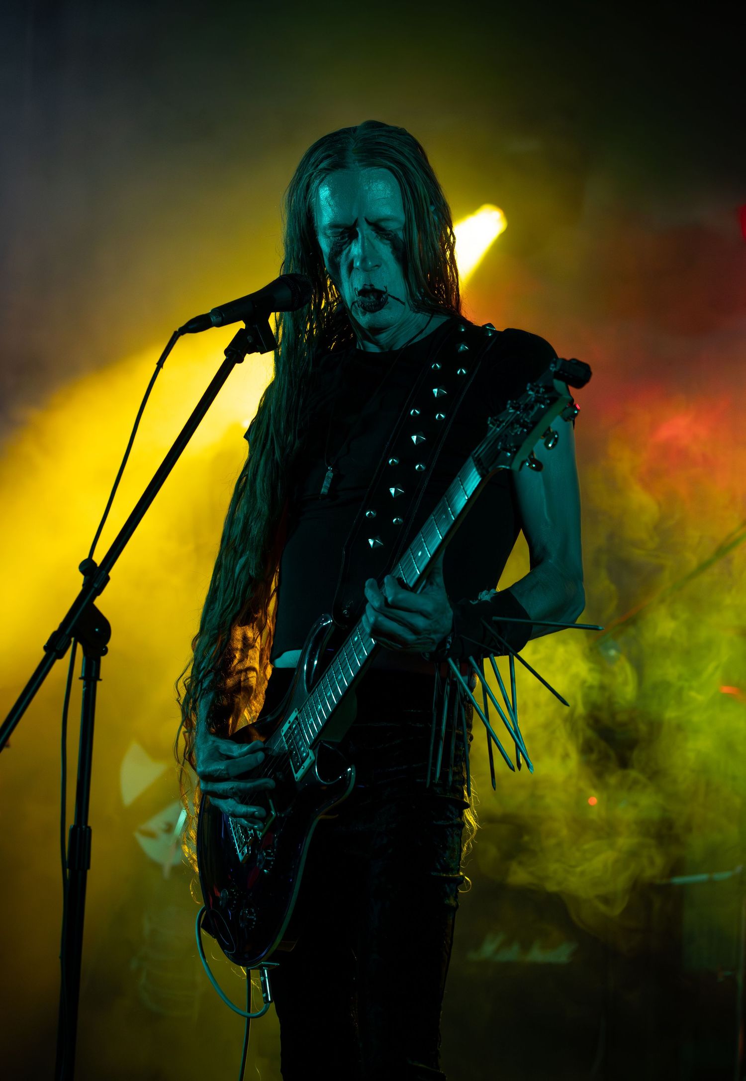 A silhouetted musician performs on stage with colorful green and yellow smoke effects in dramatic lighting.