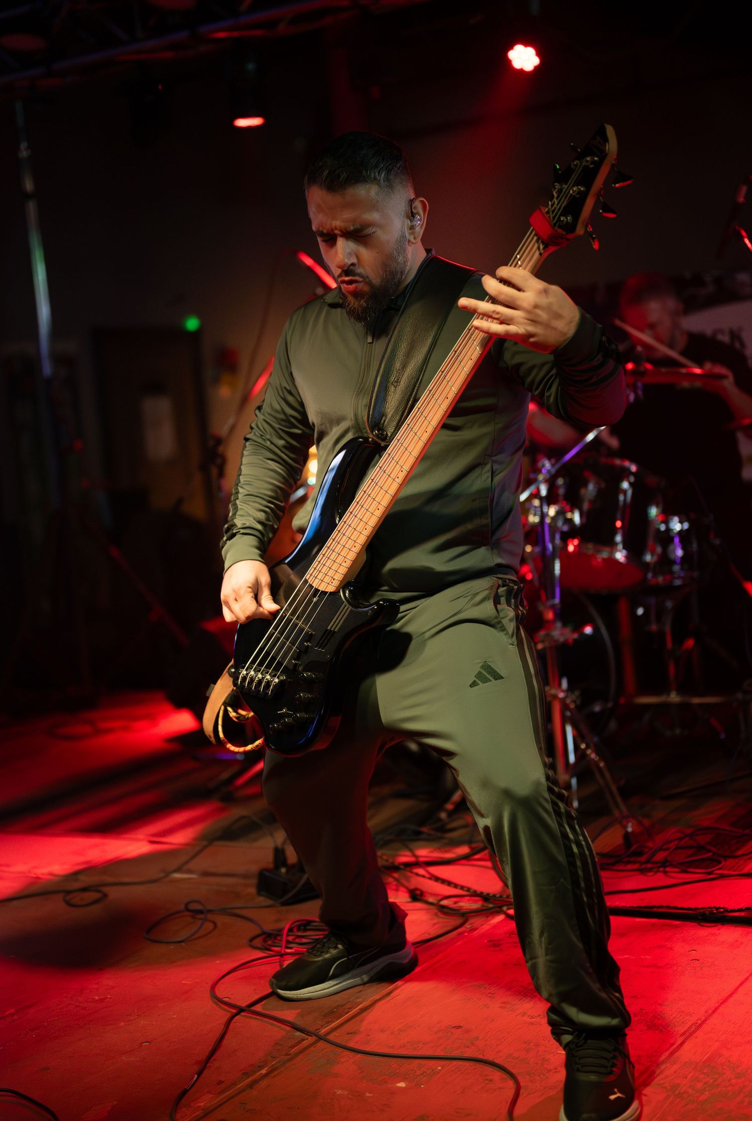 Musician performs on bass guitar under dramatic red stage lighting at live concert venue.