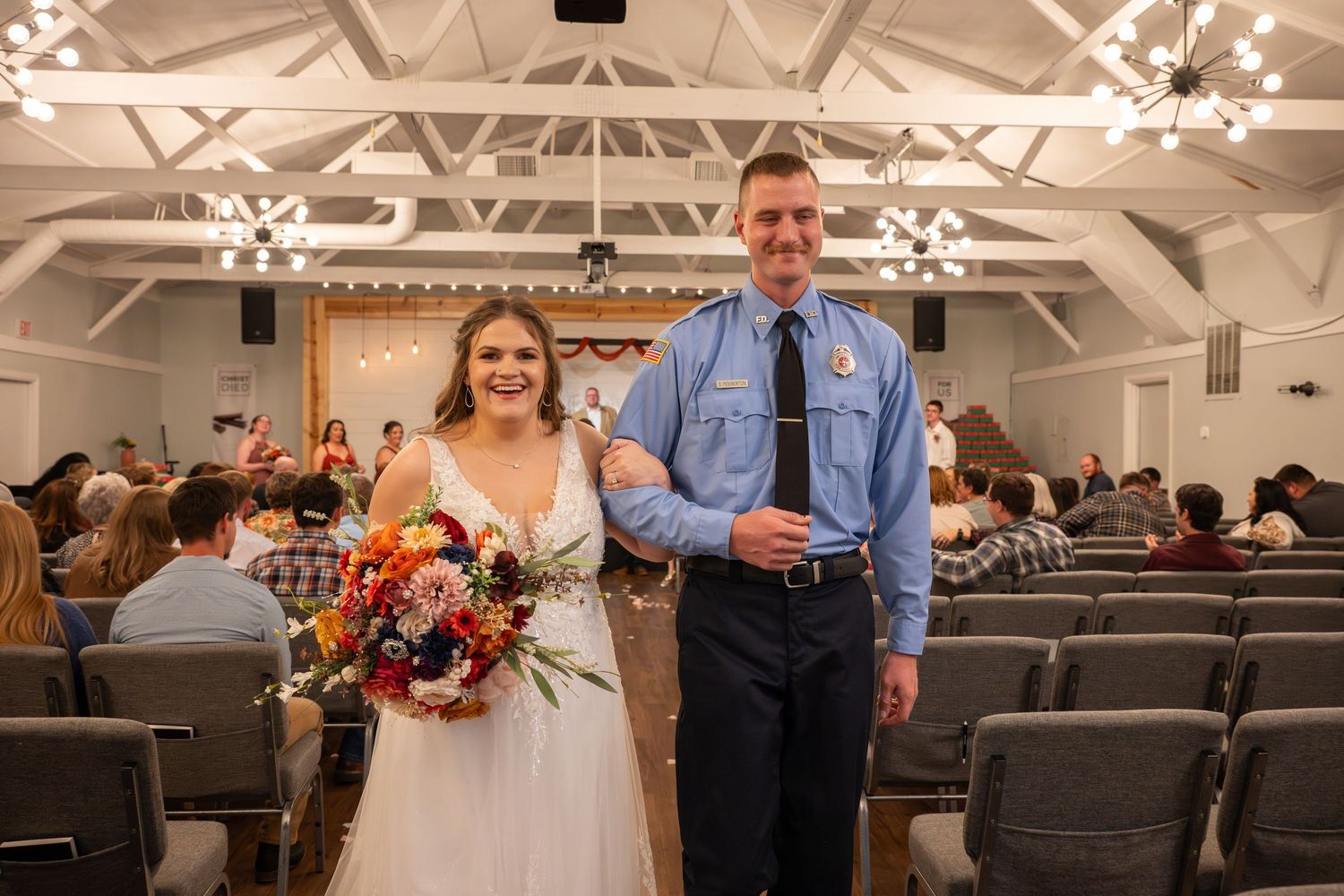 Wedding venue interior with exposed beam ceiling and rows of grey chairs.