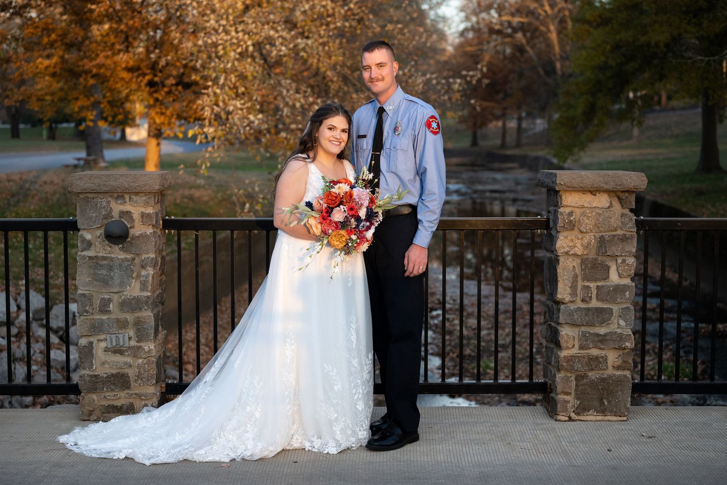 Wedding portraits taken on stone bridge during fall season with colorful foliage.