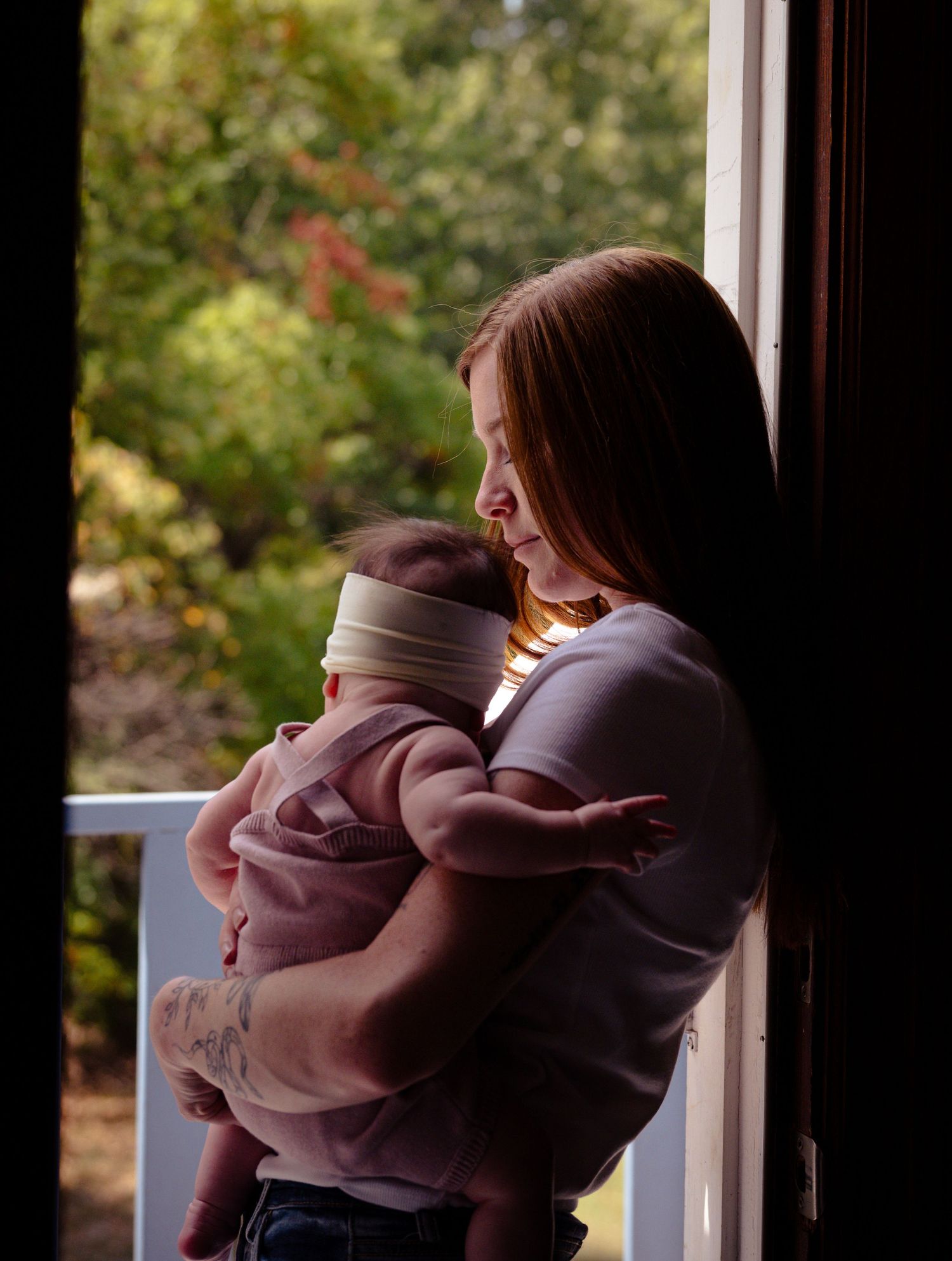 A parent and child share a tender moment while looking out a window together in matching mauve hooded sweatshirts.